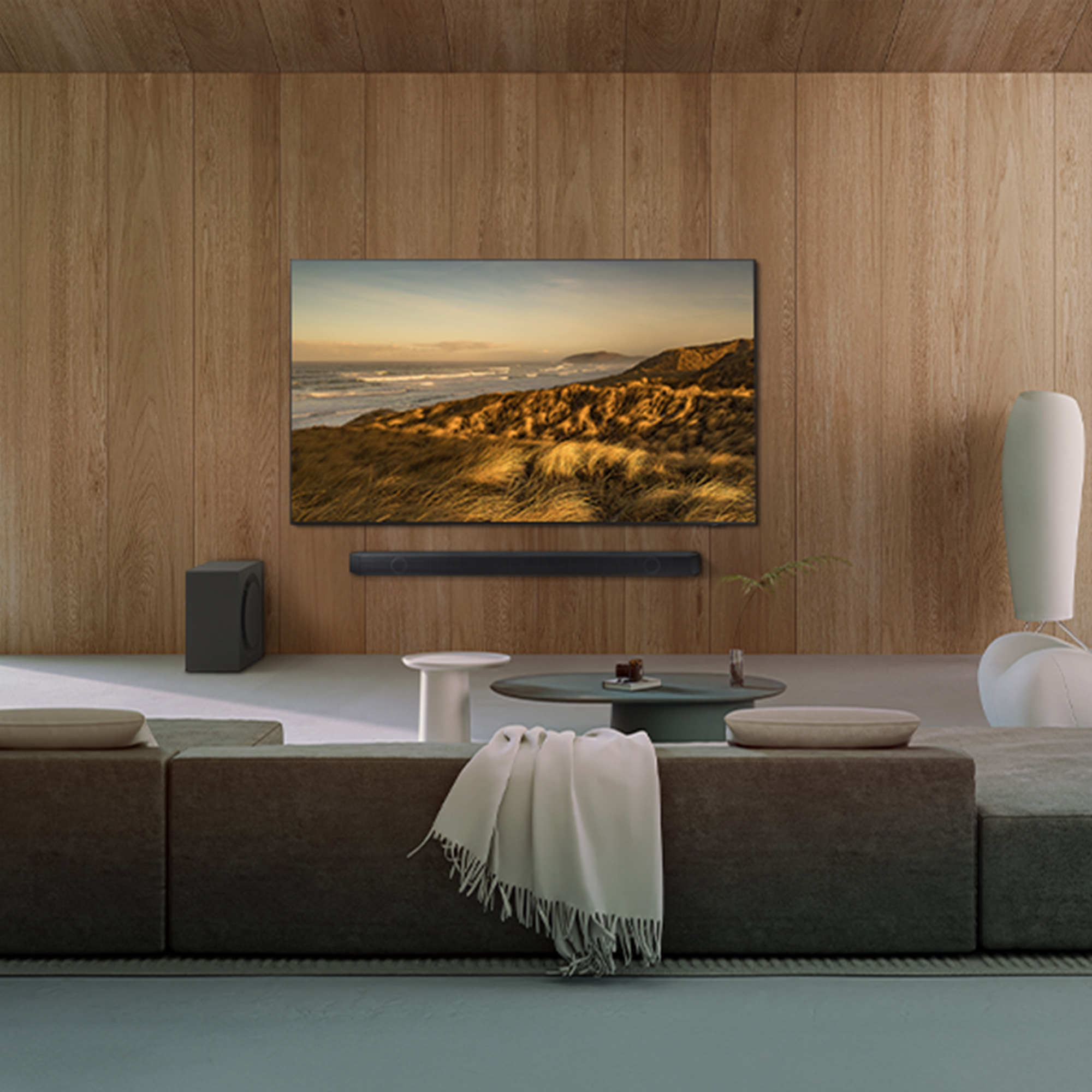 Salón con televisor de pantalla grande, barra de sonido y subwoofer. Sofá marrón, mesas auxiliares y un ambiente acogedor.
