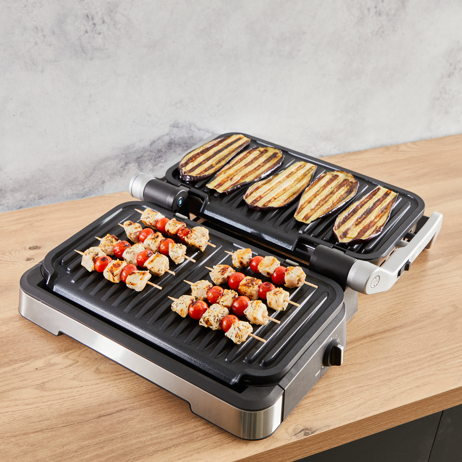 Elektromos grill grillezett nyársakkal és szeletelt padlizsánnal fa felületen.