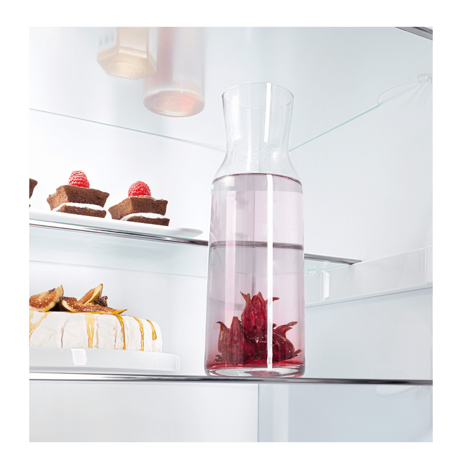 Glass pitcher with red liquid and a few items on a shelf. White background.