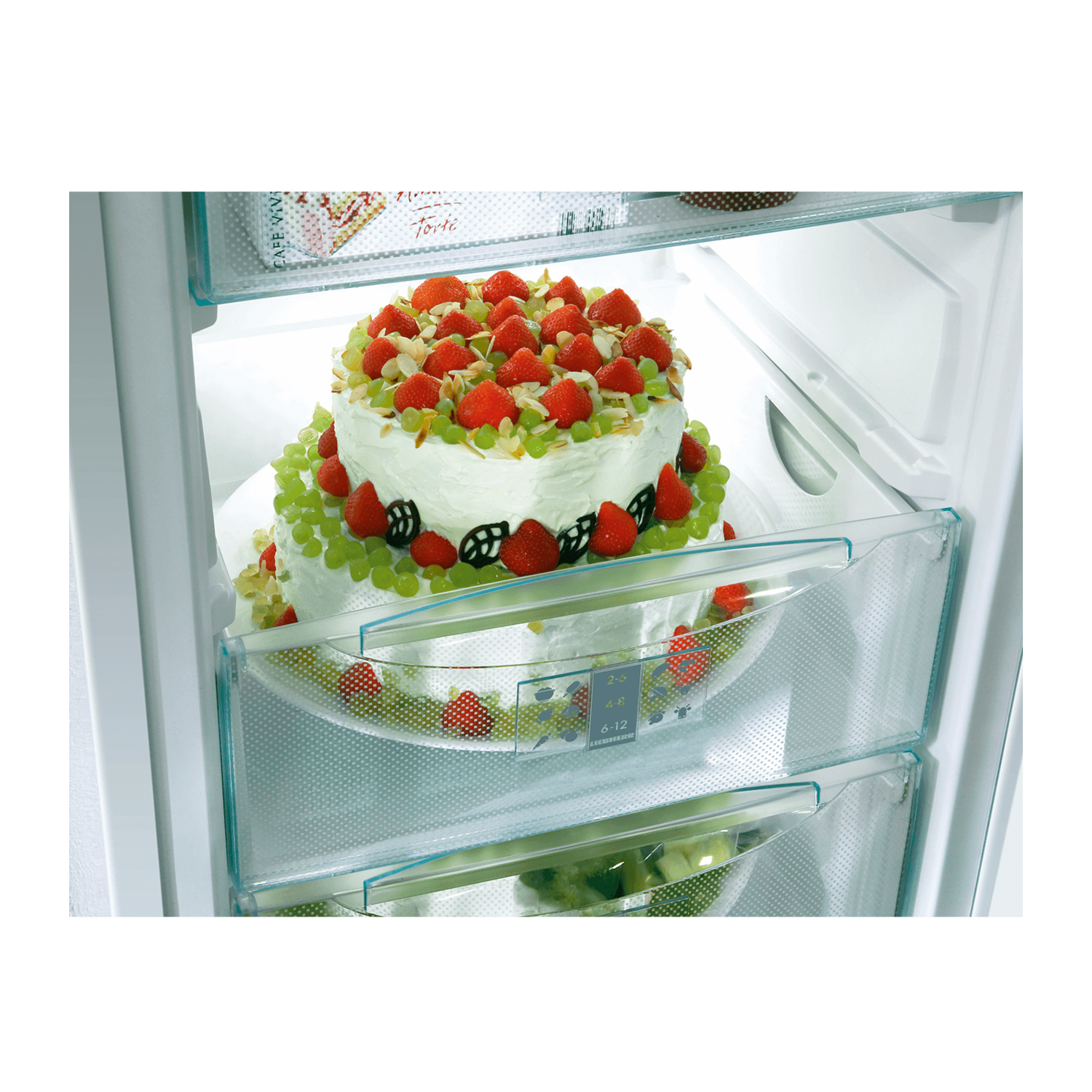 Cake in a fridge with strawberries and grapes, in clear drawers.