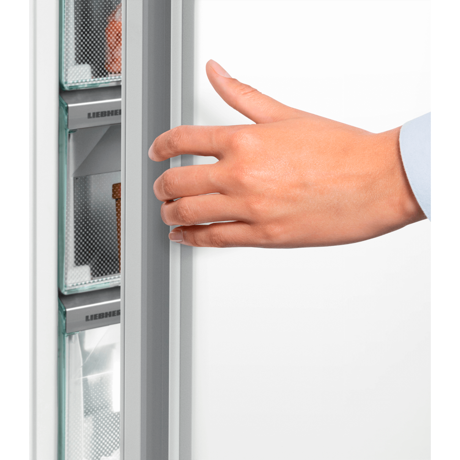 A hand reaching into a refrigerator with clear drawers.