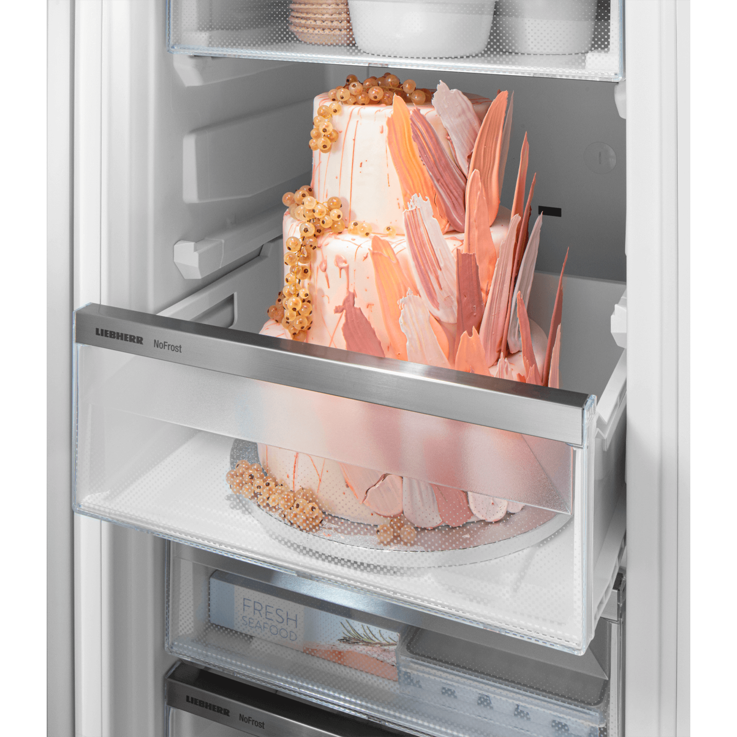 A two-tiered cake inside a refrigerator, with a drawer open.
