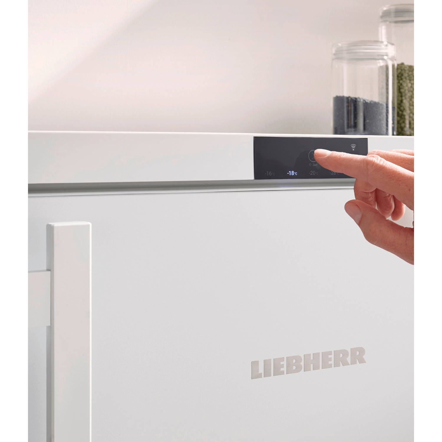 A close-up of a white freezer door with a hand pressing a button on the control panel.