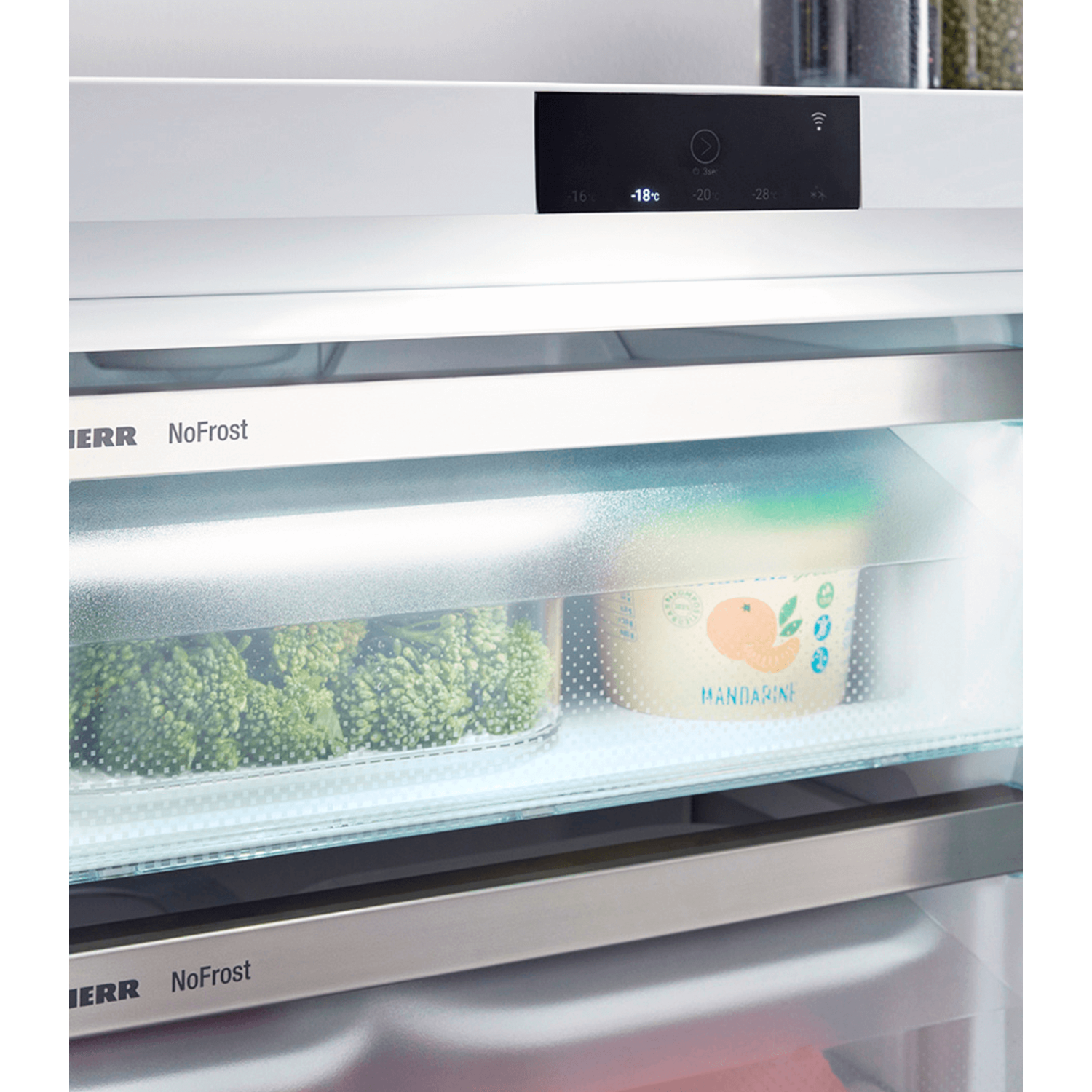 Close up of a refrigerator interior. Shows a clear shelf with broccoli and a container of mandarin oranges.