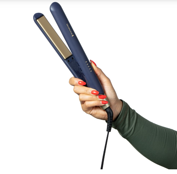 La mano de una mujer sosteniendo una plancha para el cabello azul marino y dorado con uñas rojas.