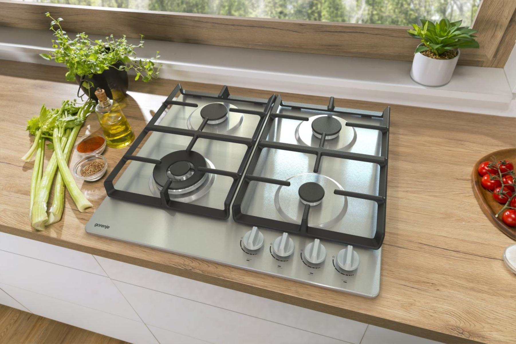 Gazowa kuchenka ze stali nierdzewnej z czterema palnikami, pokrętłami i składnikami na drewnianym blacie.