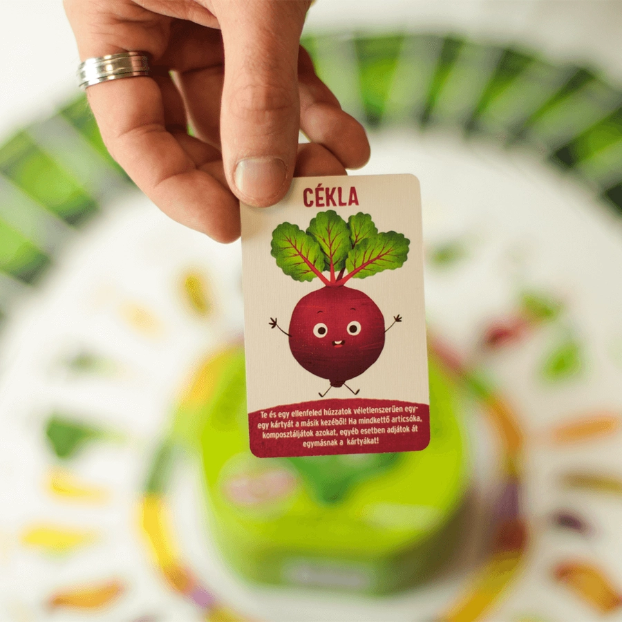 Egy kéz tart egy játékkártyát céklailusztrációval és a 'Cékla' szóval.