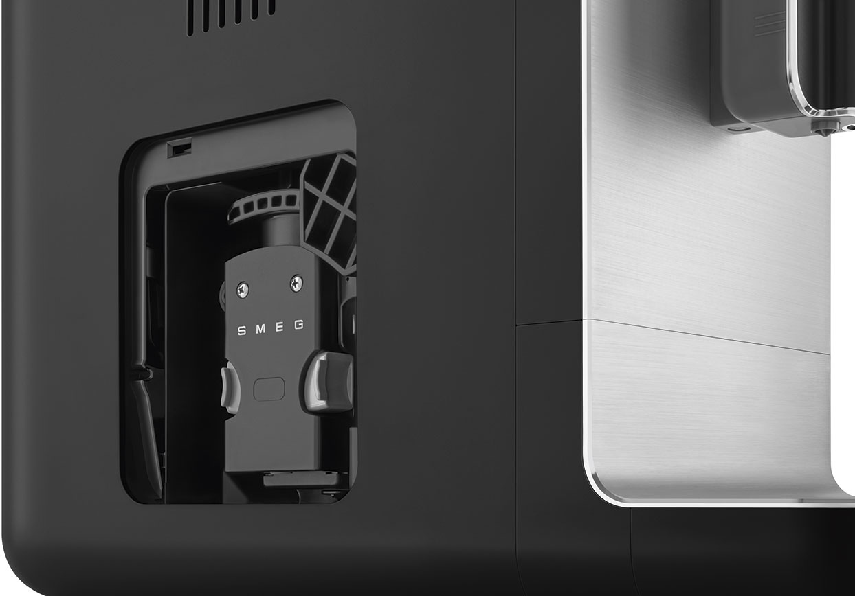 Primo piano di un componente nero di una macchina da caffè SMEG, con un accento metallico argentato. Su sfondo bianco.