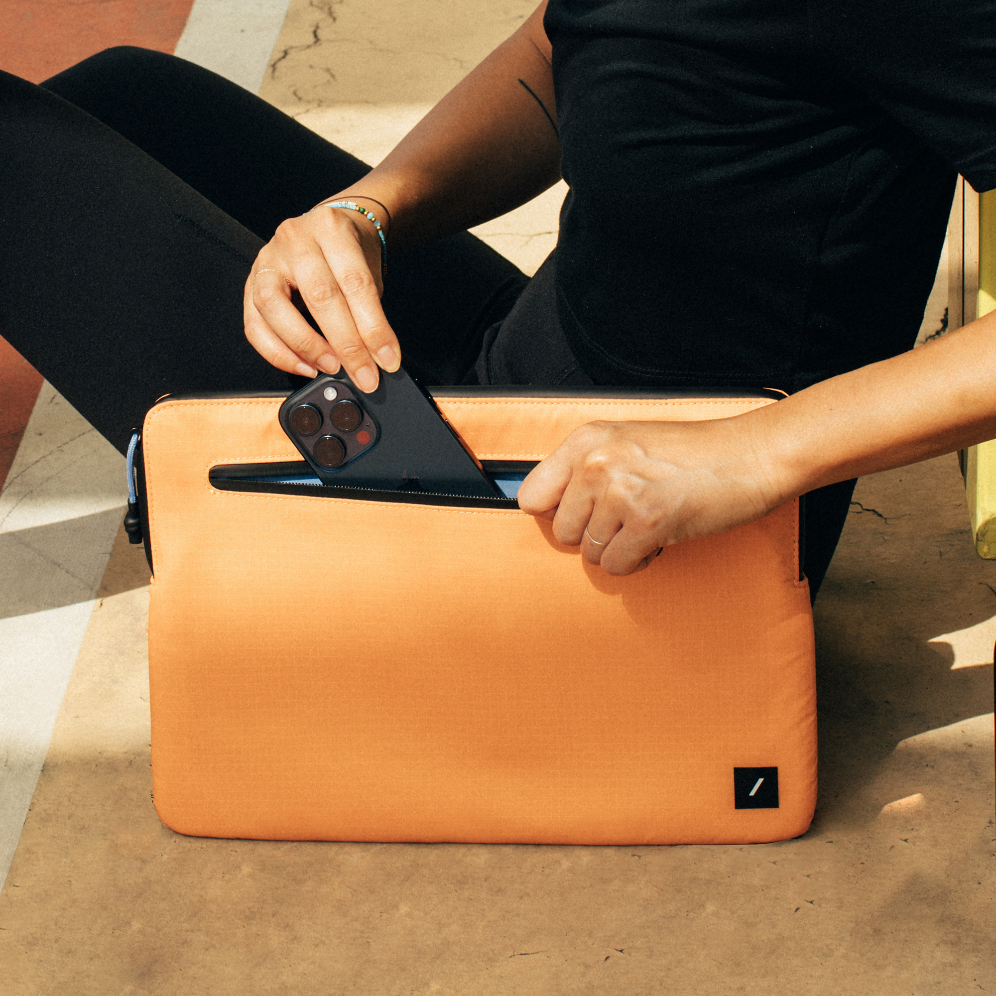 Eine Person, die ein Telefon in eine orangefarbene, mit Reißverschluss versehene Hülle legt.