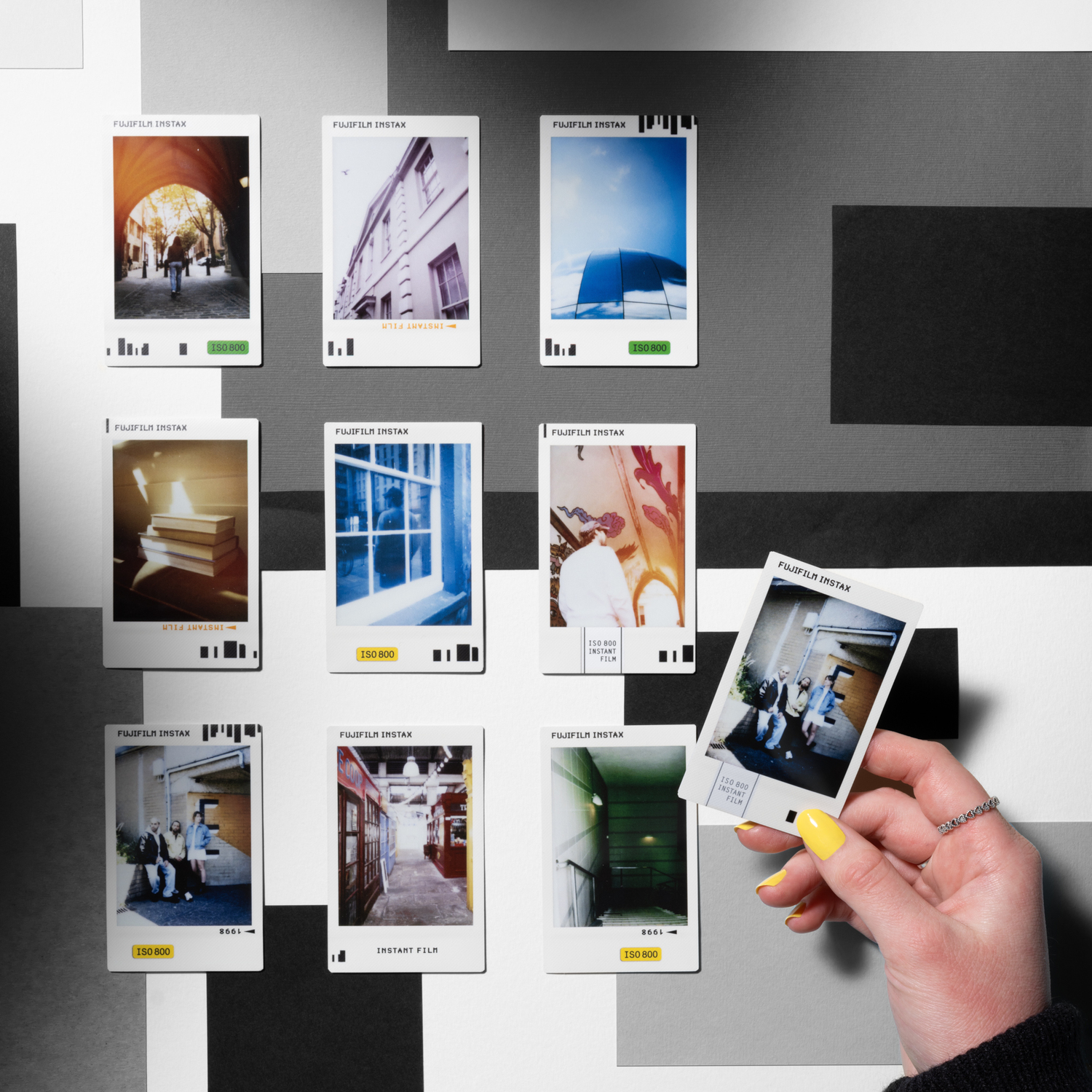 Polaroid photos on a wall. A hand is holding one, with yellow nails.