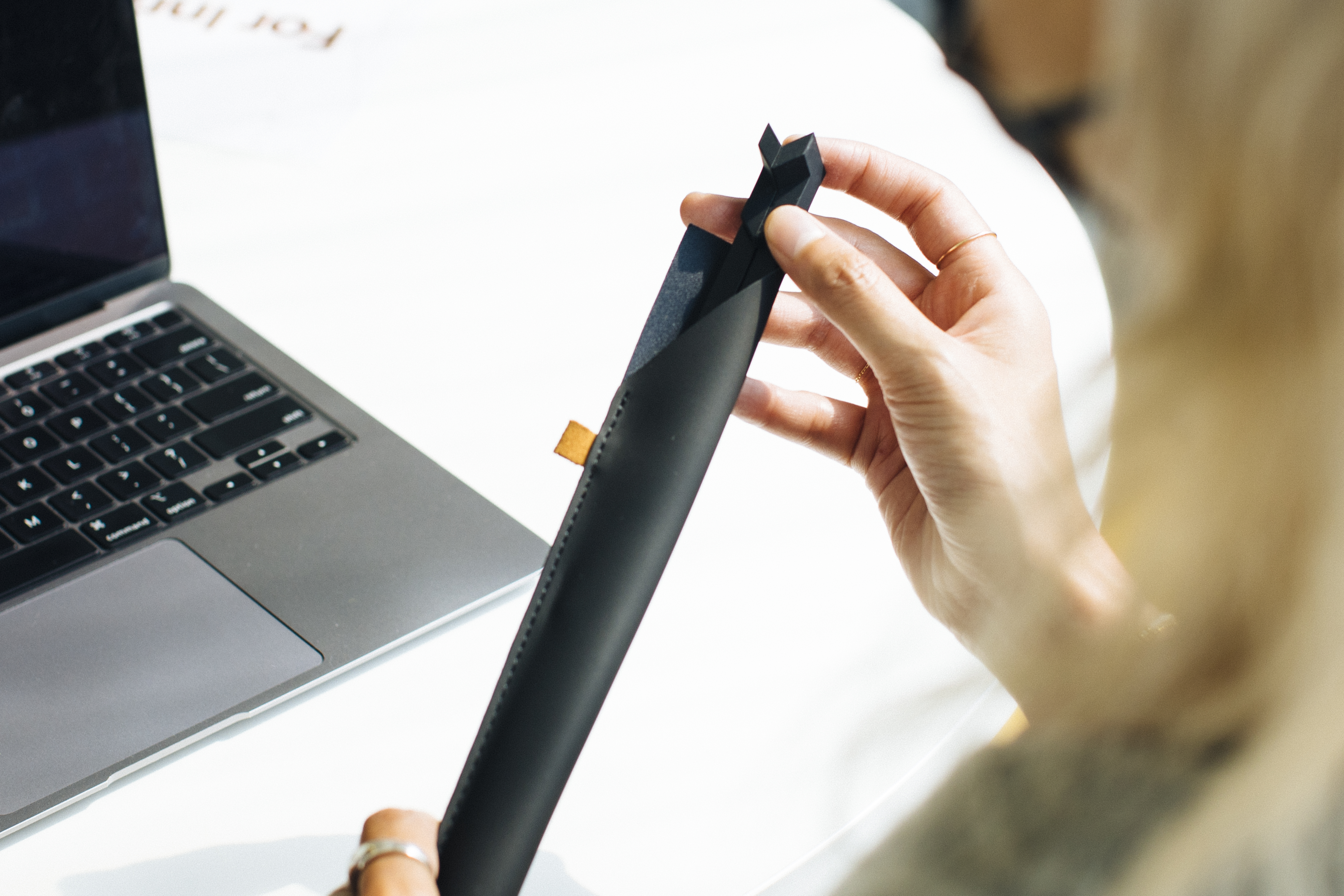 Eine Person, die ein schwarzes Werkzeug in der Nähe eines Laptops auf einem weißen Tisch hält, mit verschwommenem Hintergrund.