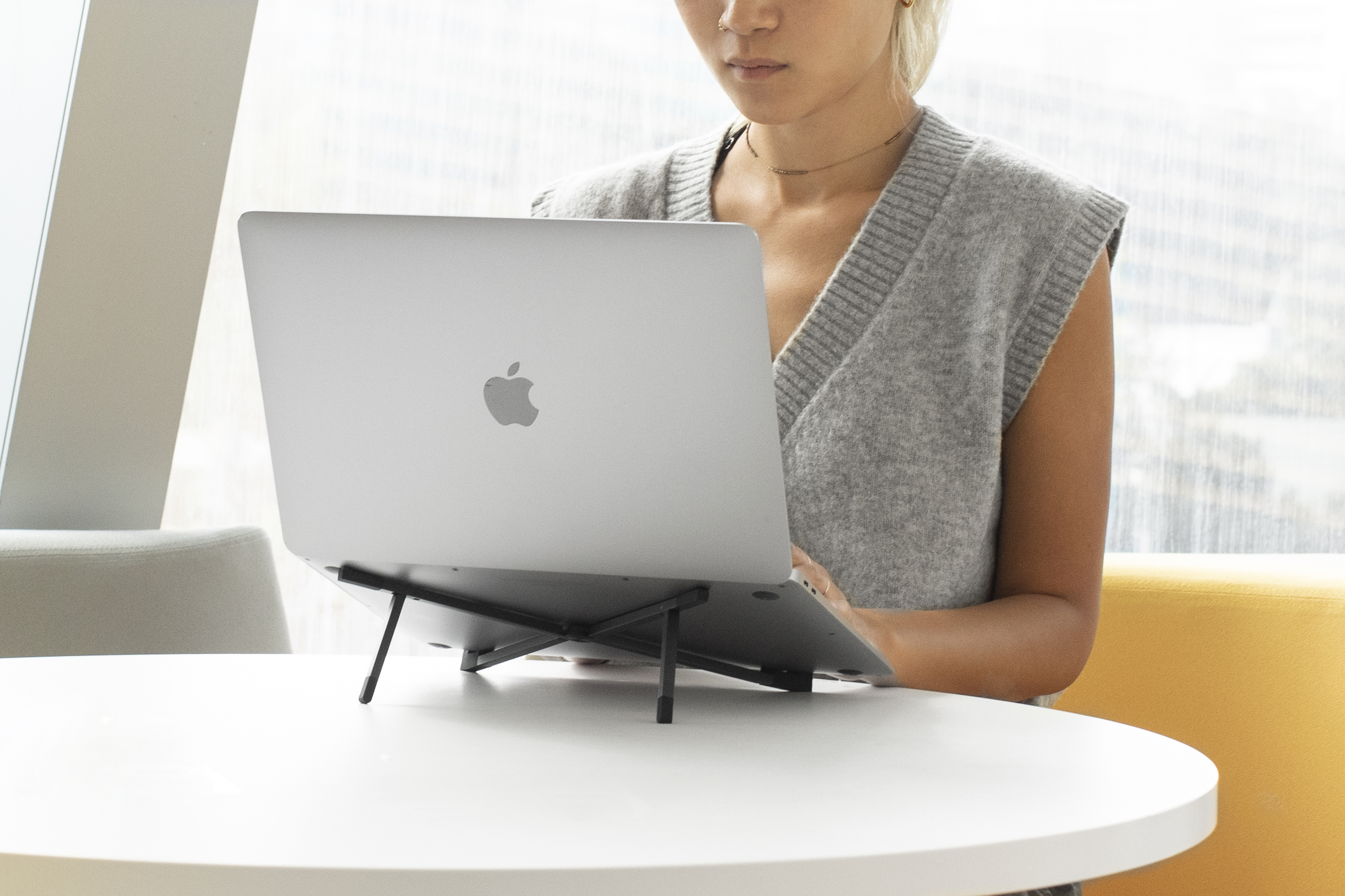 Eine Frau, die einen Laptop auf einem Ständer auf einem weißen Tisch benutzt.
