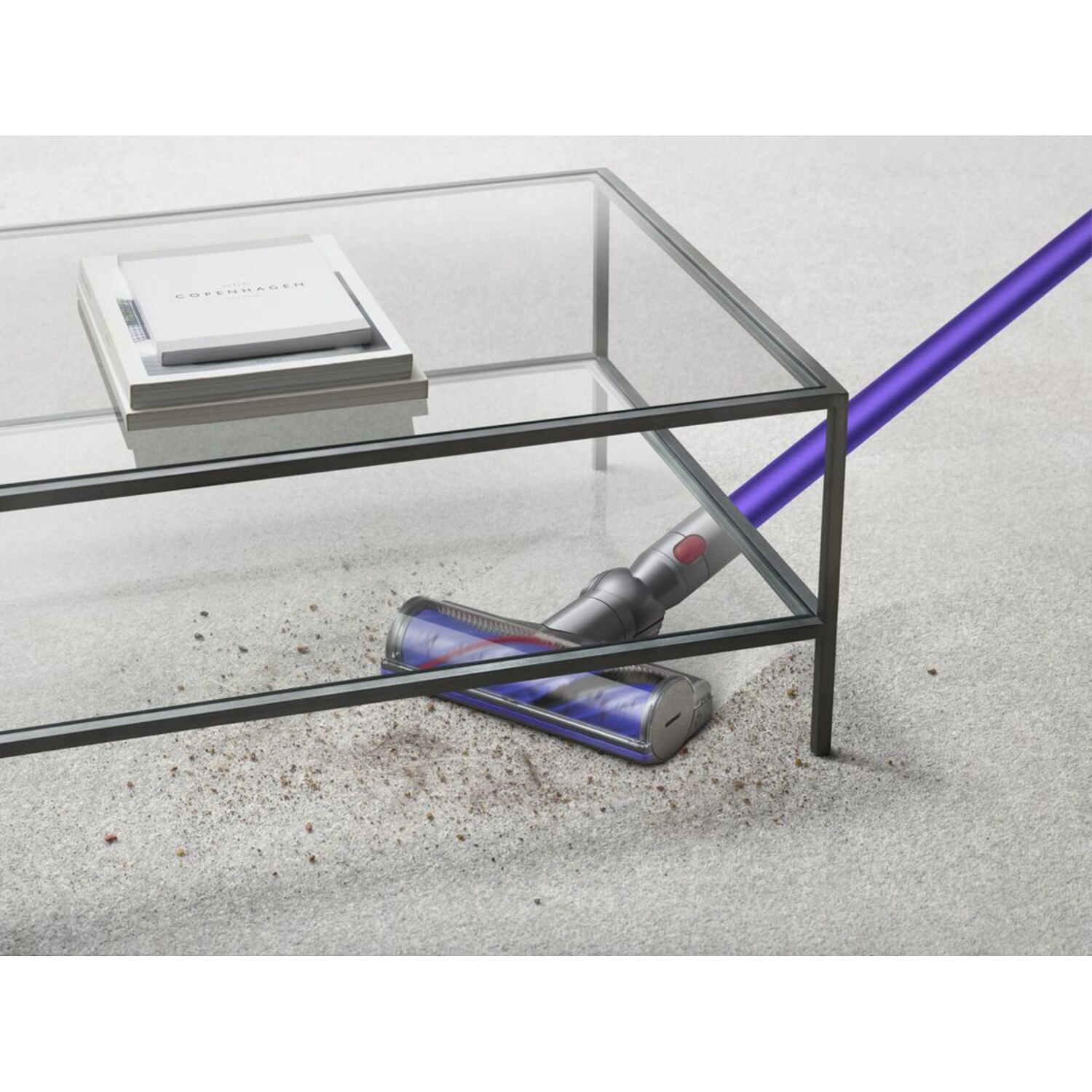 Aspirateur avec un tube violet nettoyant un tapis. Une table en verre avec des livres est en arrière-plan.
