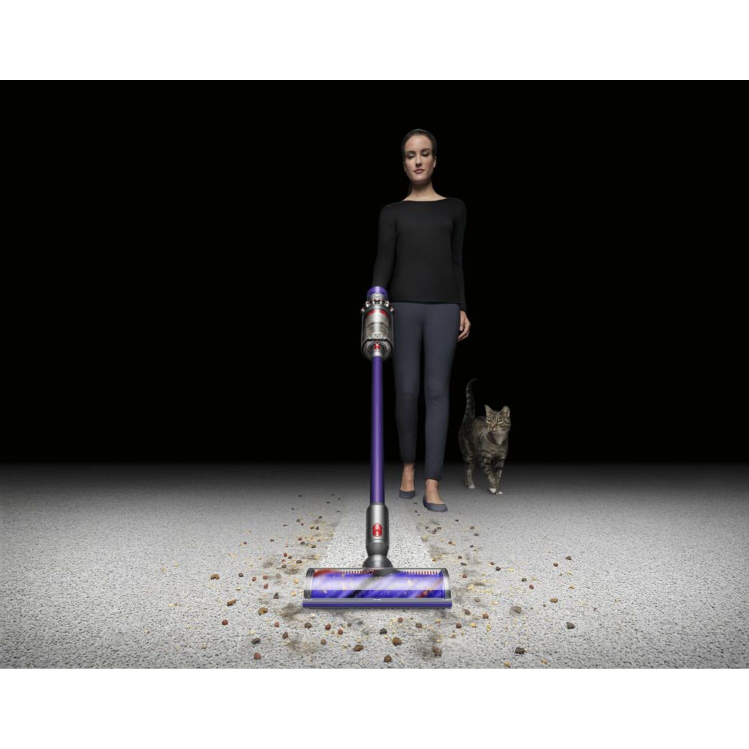 Une femme passe l'aspirateur sur un sol sale avec un aspirateur, et un chat est à proximité.