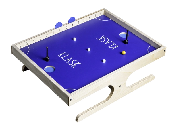 Egy Klask játéktábla fehér háttéren. Kék, fehér betűkkel, játékelemekkel.