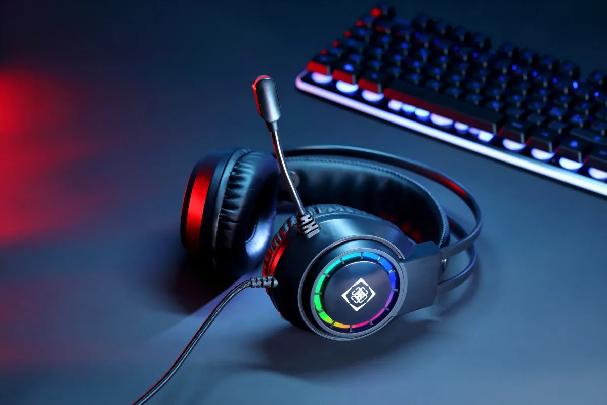 Cuffie da gioco con microfono e illuminazione RGB su una superficie scura con una tastiera sullo sfondo.