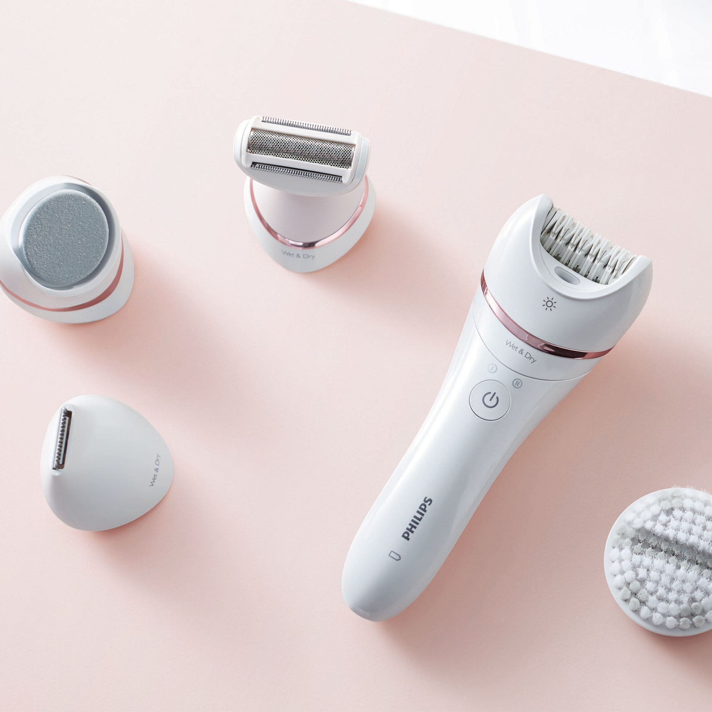 Biały depilator i nasadki ułożone na różowym tle.