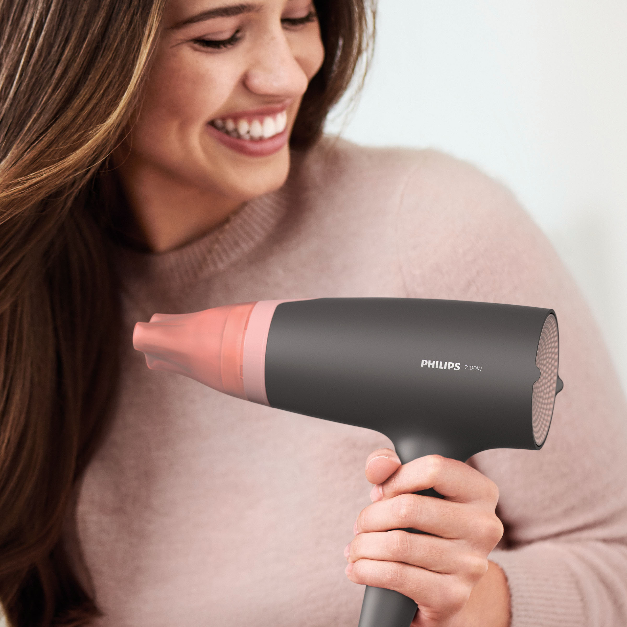 Kobieta używająca ciemnoszarej i różowej suszarki Philips. Uśmiecha się, włosy są częściowo wysuszone.