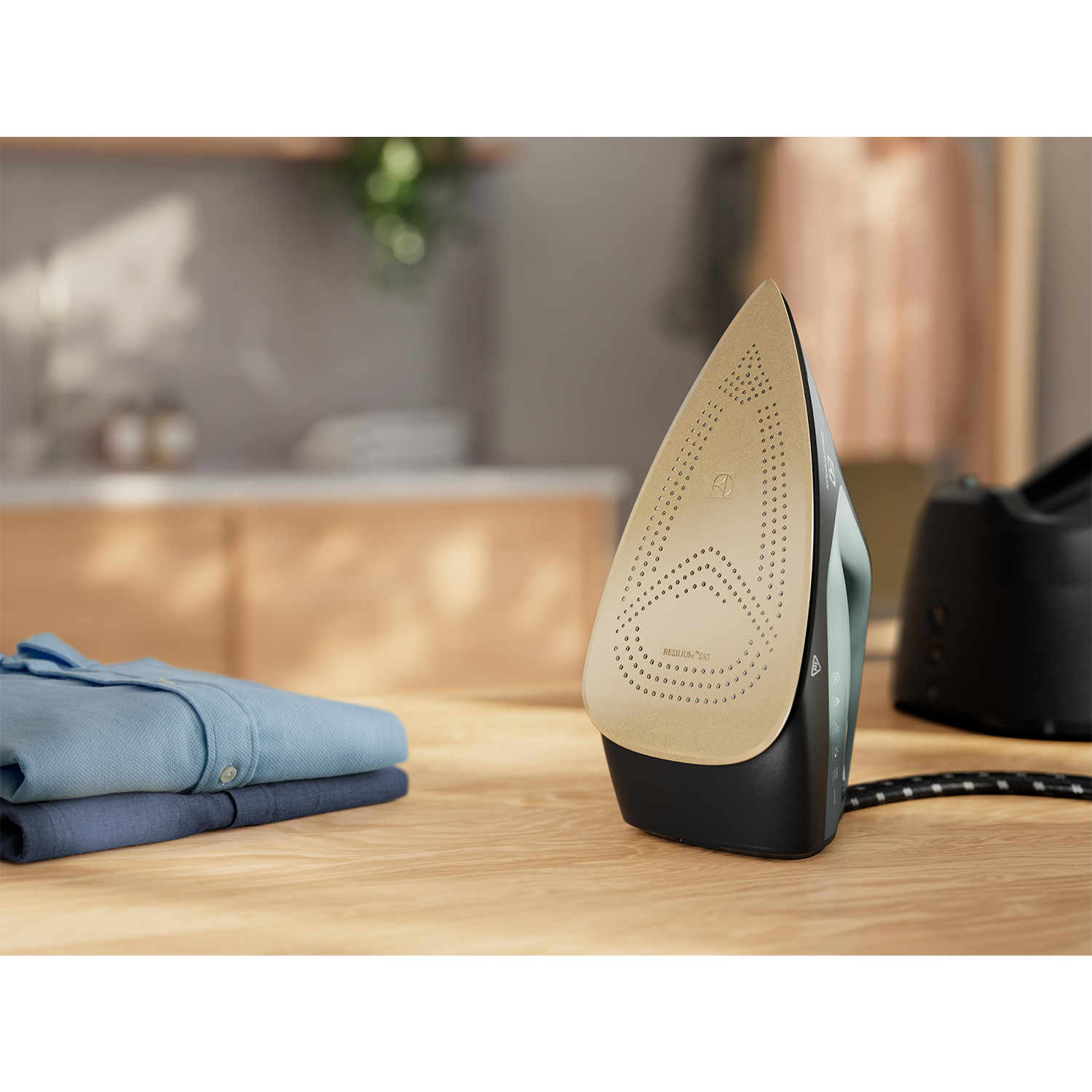 Un ferro da stiro con base color oro su un tavolo di legno accanto ai vestiti.