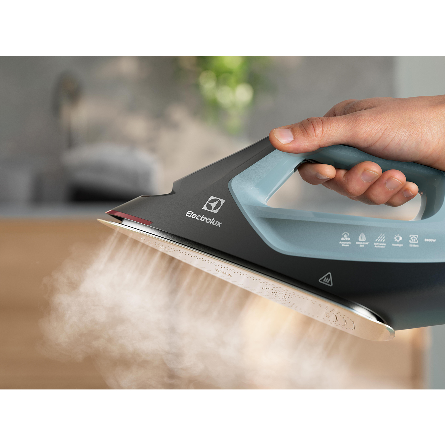 Ferro da stiro a vapore. Mano che tiene il ferro. Logo Electrolux visibile.