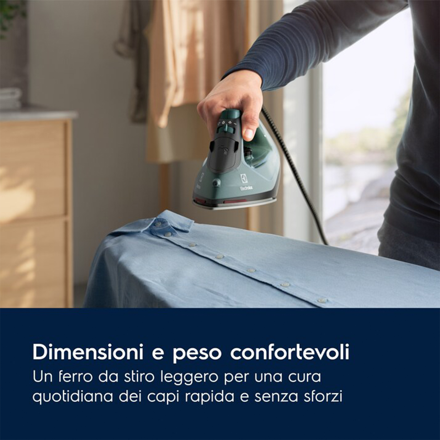 Una persona che stira una camicia azzurra. Il ferro è verde e l'asse da stiro bianca.