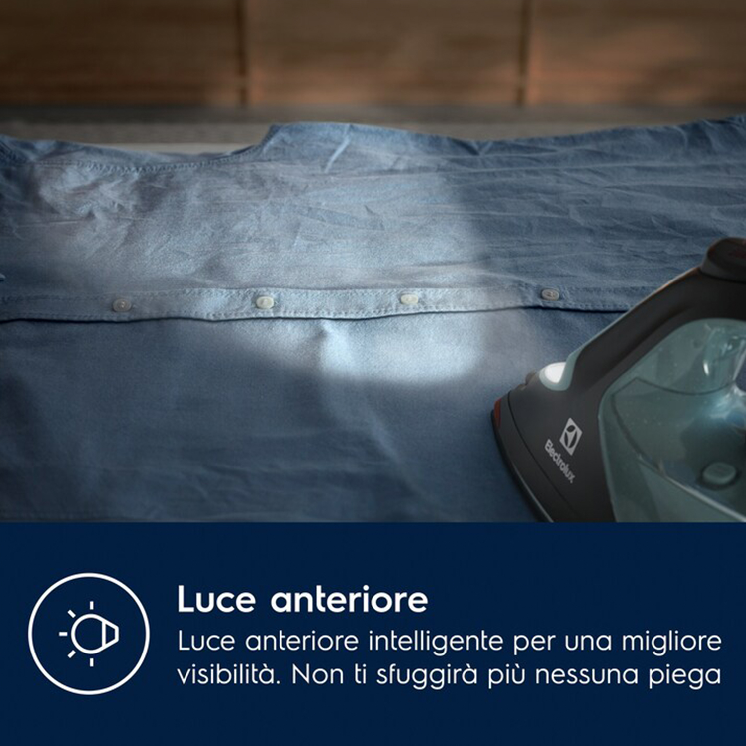 Un ferro da stiro sta stirando una camicia blu su un tavolo di legno. Il ferro è nero e grigio.