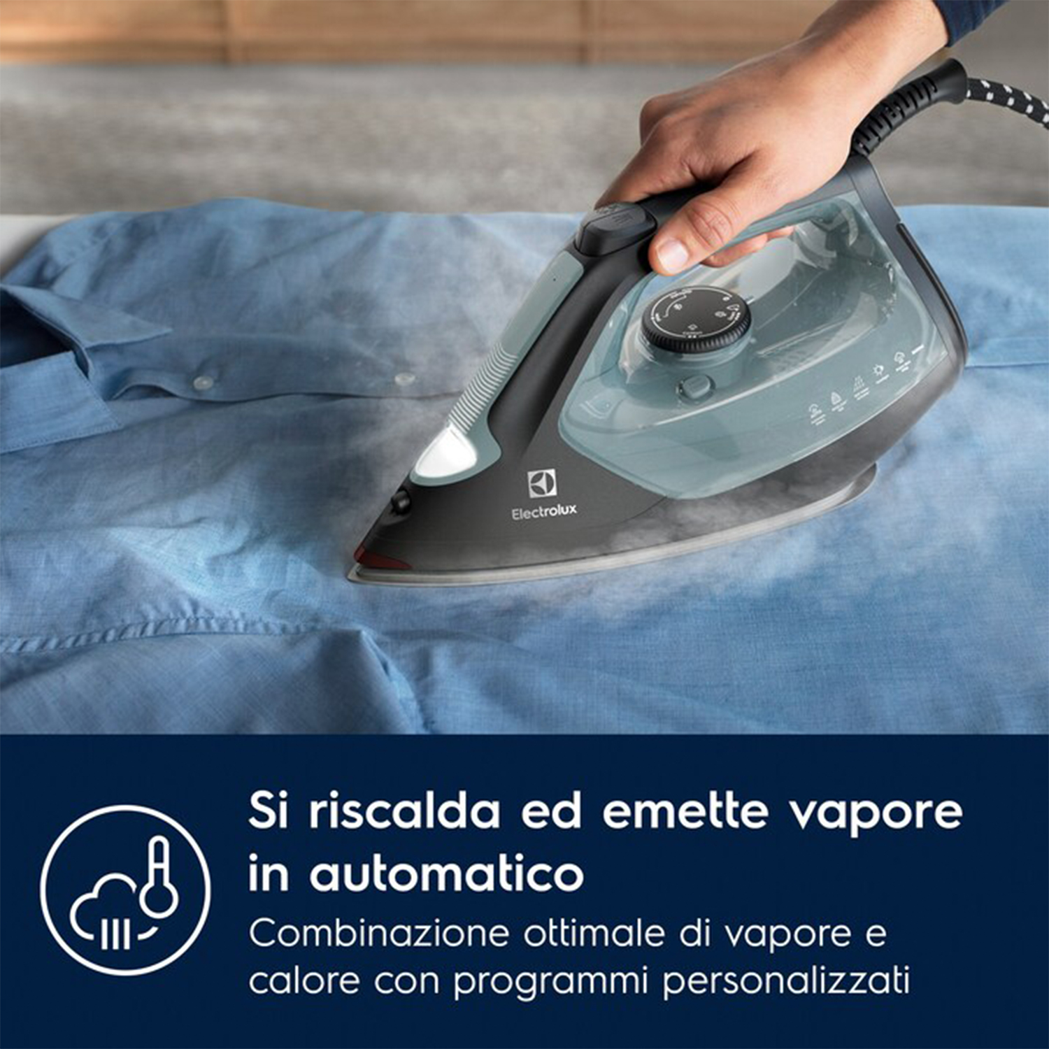 Persona che stira una camicia blu. Il ferro è nero con dettagli verde acqua, su superficie bianca.