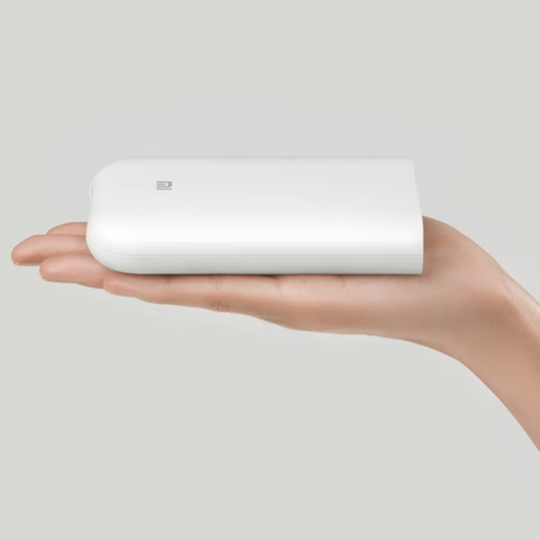 Egy fehér, téglalap alakú power bank fekszik egy kézen. A háttér világos szürke.