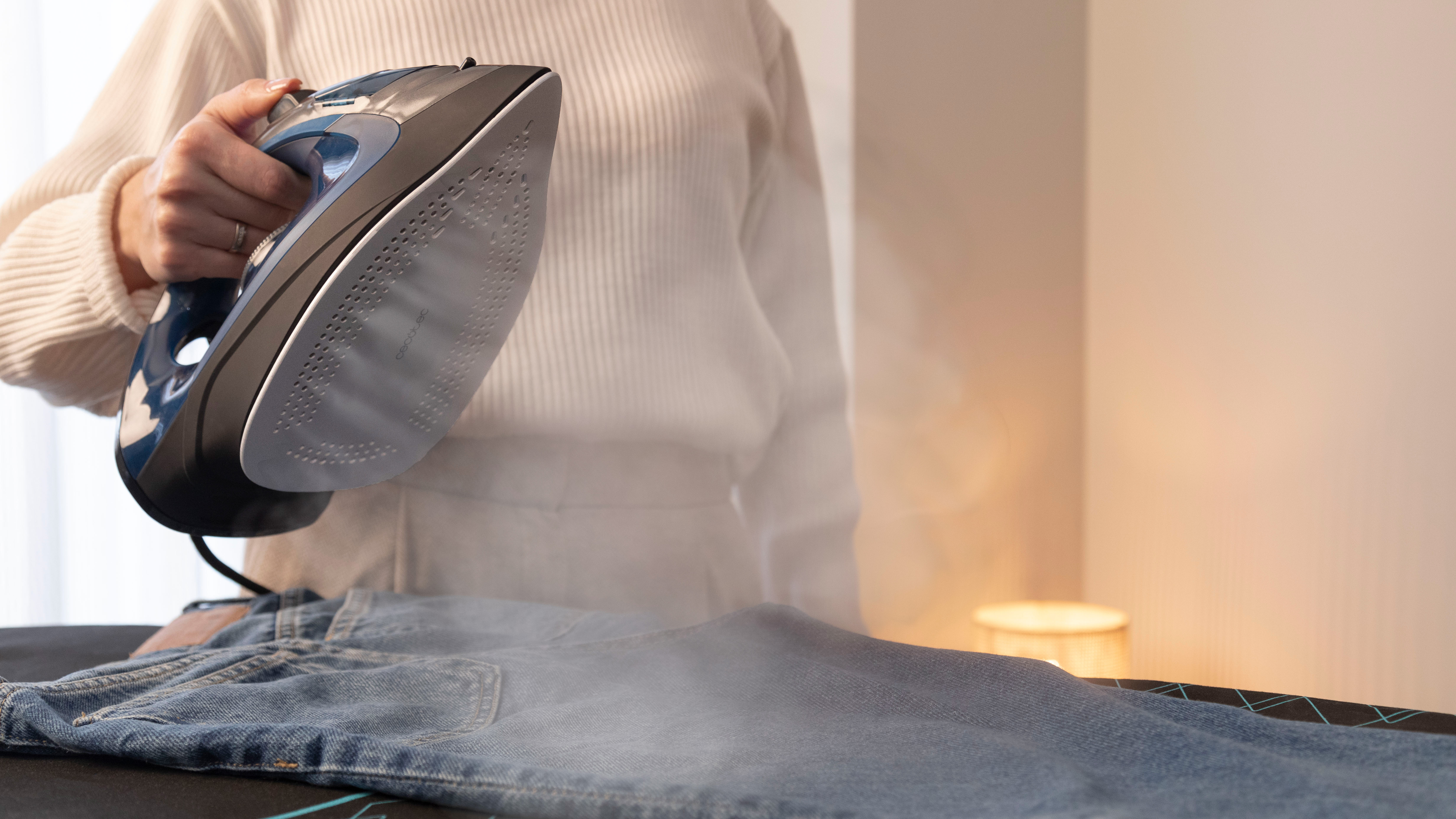 Una persona planchando unos vaqueros denim sobre una tabla de planchar, vapor saliendo de la plancha.