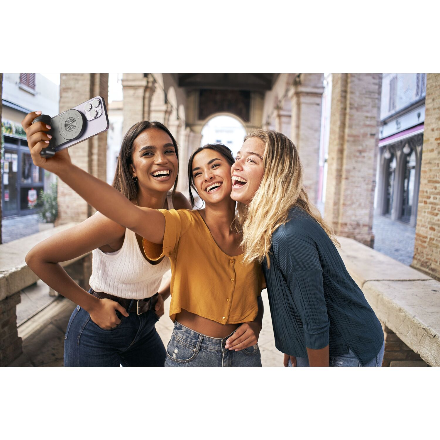 Three young women take a selfie with a phone attached to a black, circular grip.