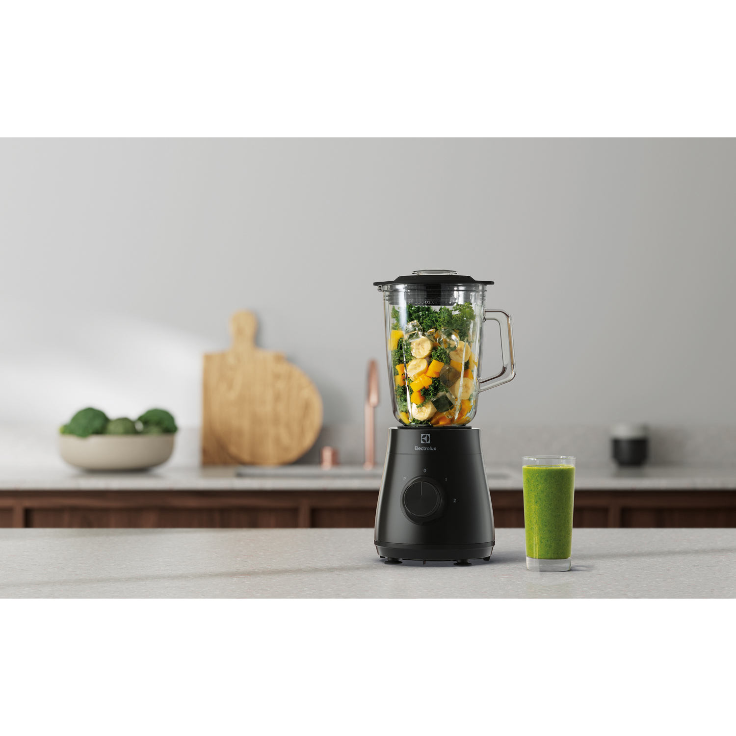Frullatore con ingredienti e un bicchiere di frullato verde sul bancone.