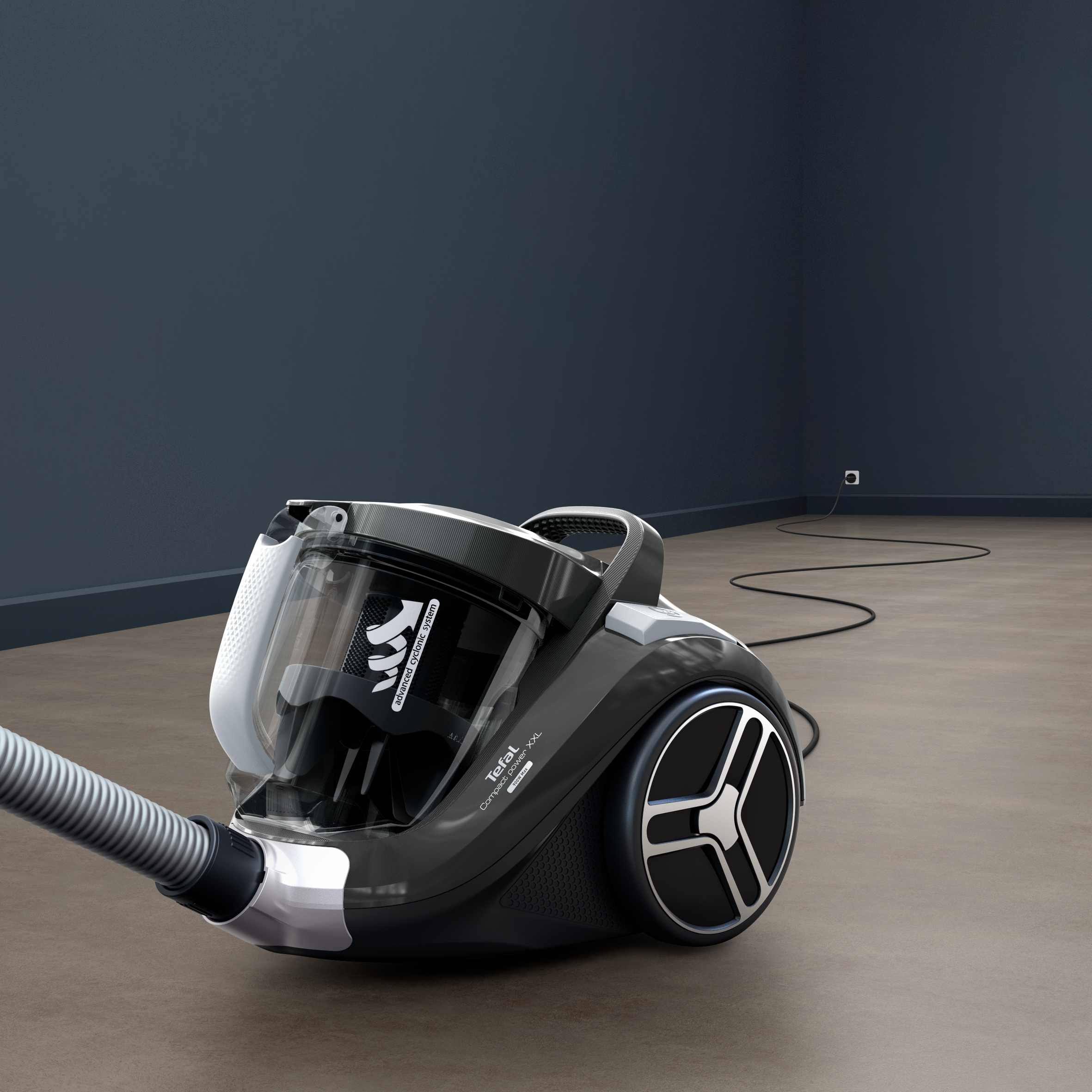 Czarny odkurzacz Tefal na brązowej podłodze, obok ciemnoniebieskiej ściany. Wąż jest rozciągnięty.