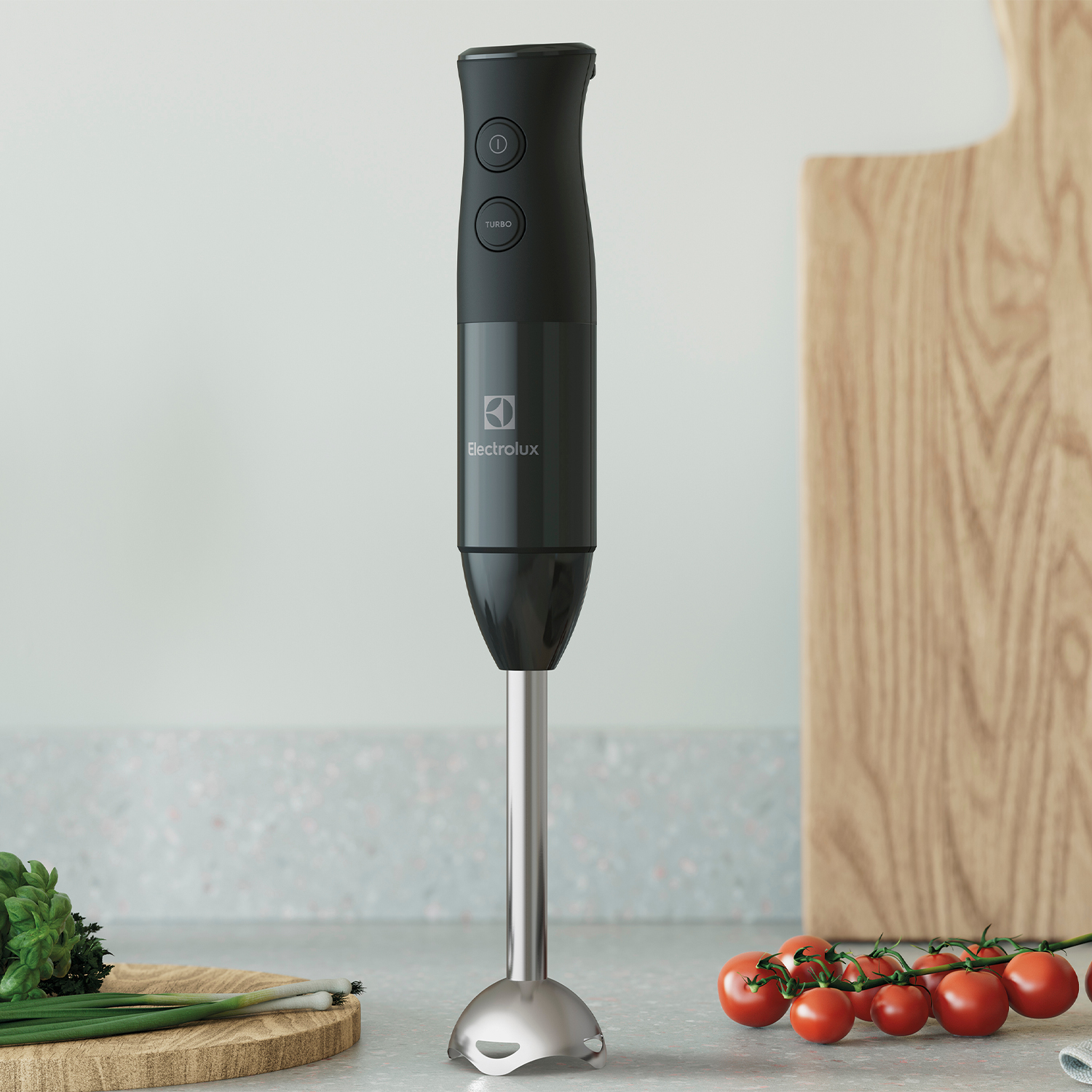 Un frullatore a immersione Electrolux nero su un bancone, con verdure e pomodori.