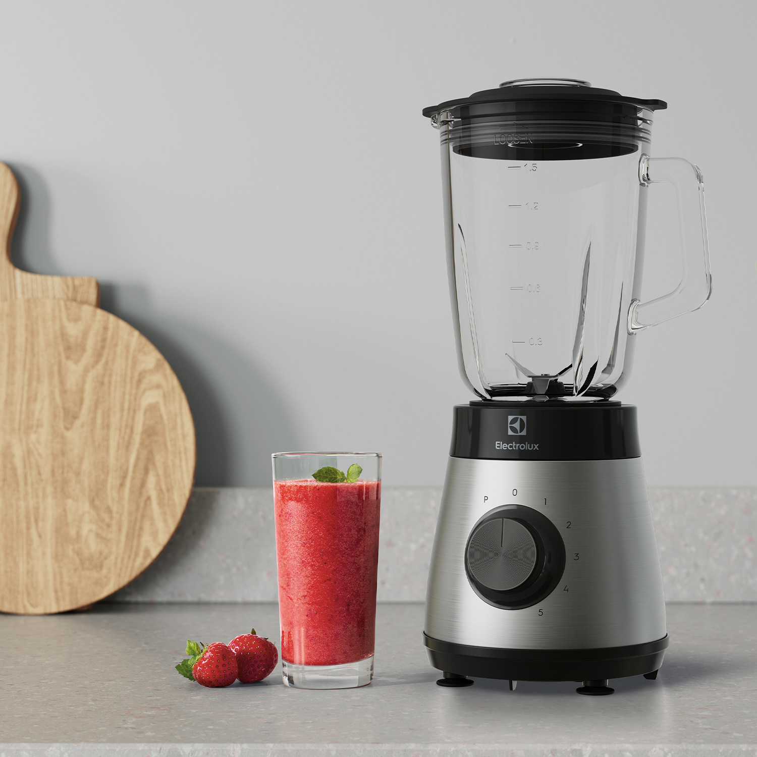 Un frullatore Electrolux su un piano di lavoro con un bicchiere di frullato rosso, un tagliere di legno e fragole.