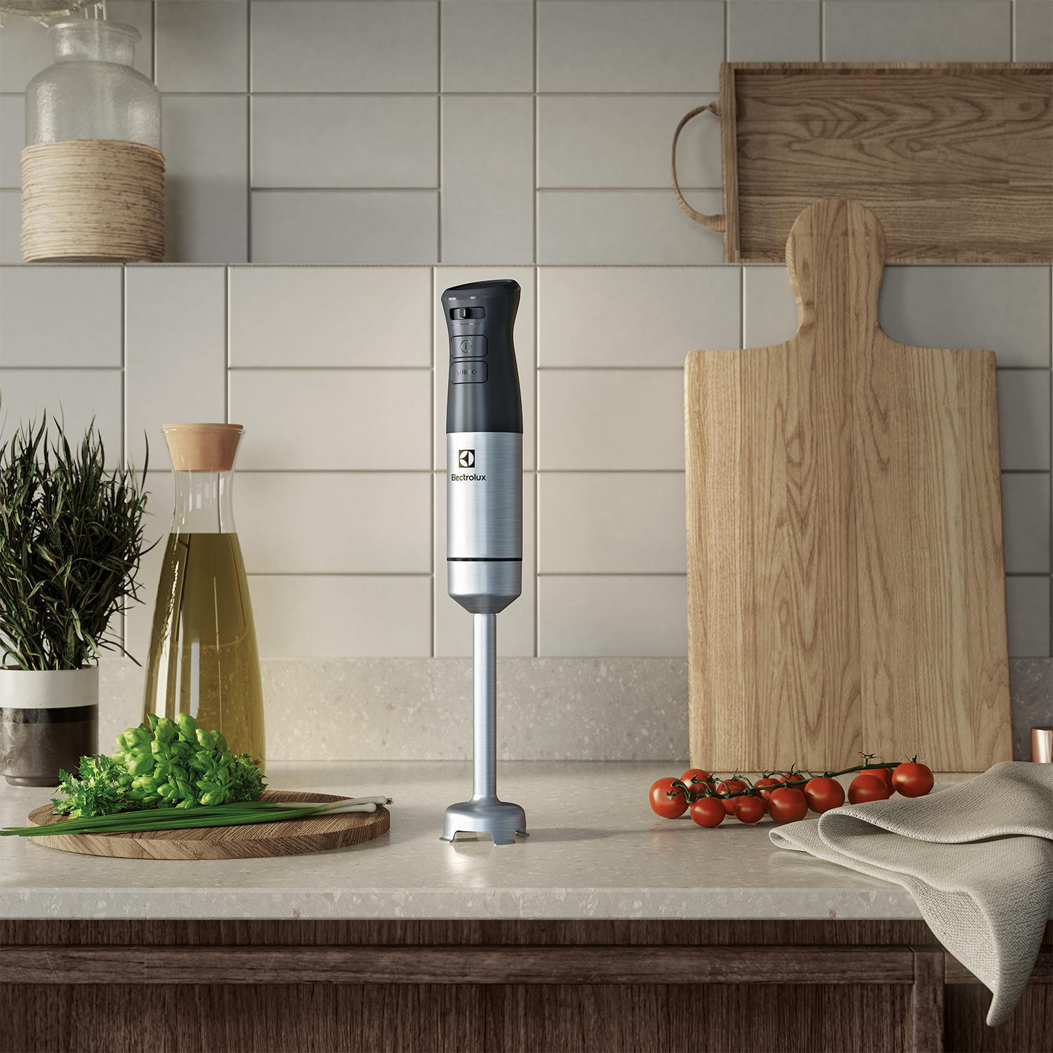 Un frullatore a immersione argento e nero è appoggiato su un piano di lavoro, con verdure, pomodori e un tagliere in legno.