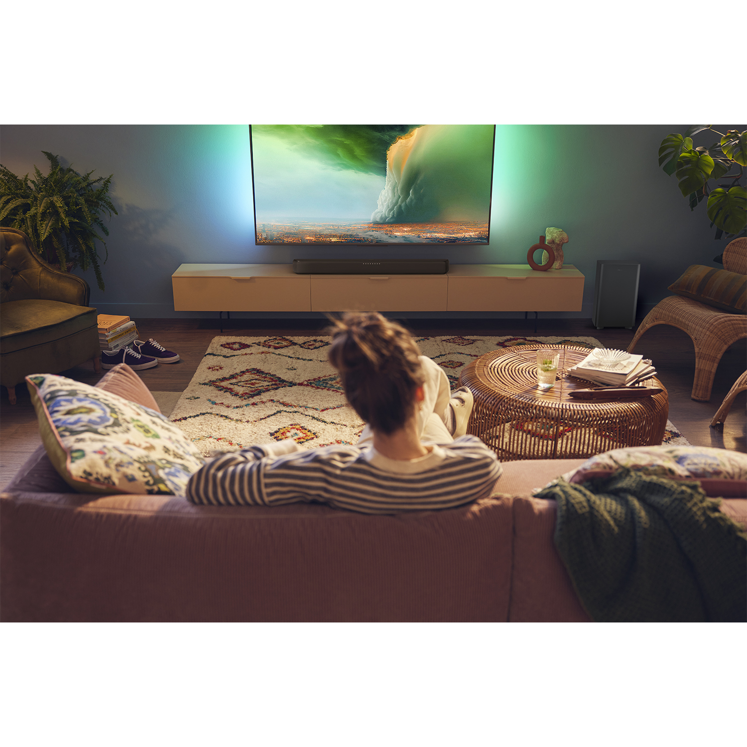 Persona guarda la TV. TV su un supporto, soundbar sotto. Soggiorno moderno.