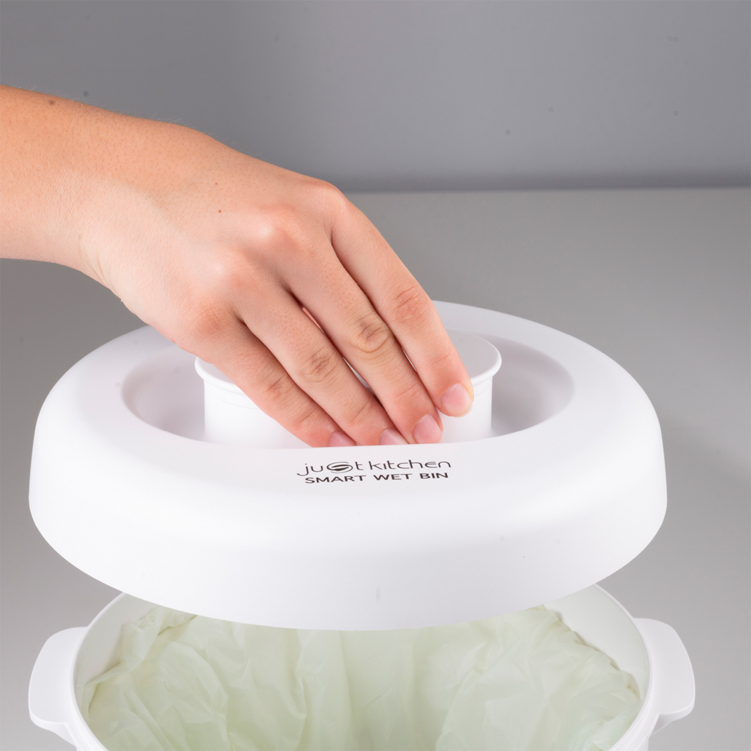 Mano che mette un coperchio su un bidone umido intelligente bianco con un sacco della spazzatura all'interno.
