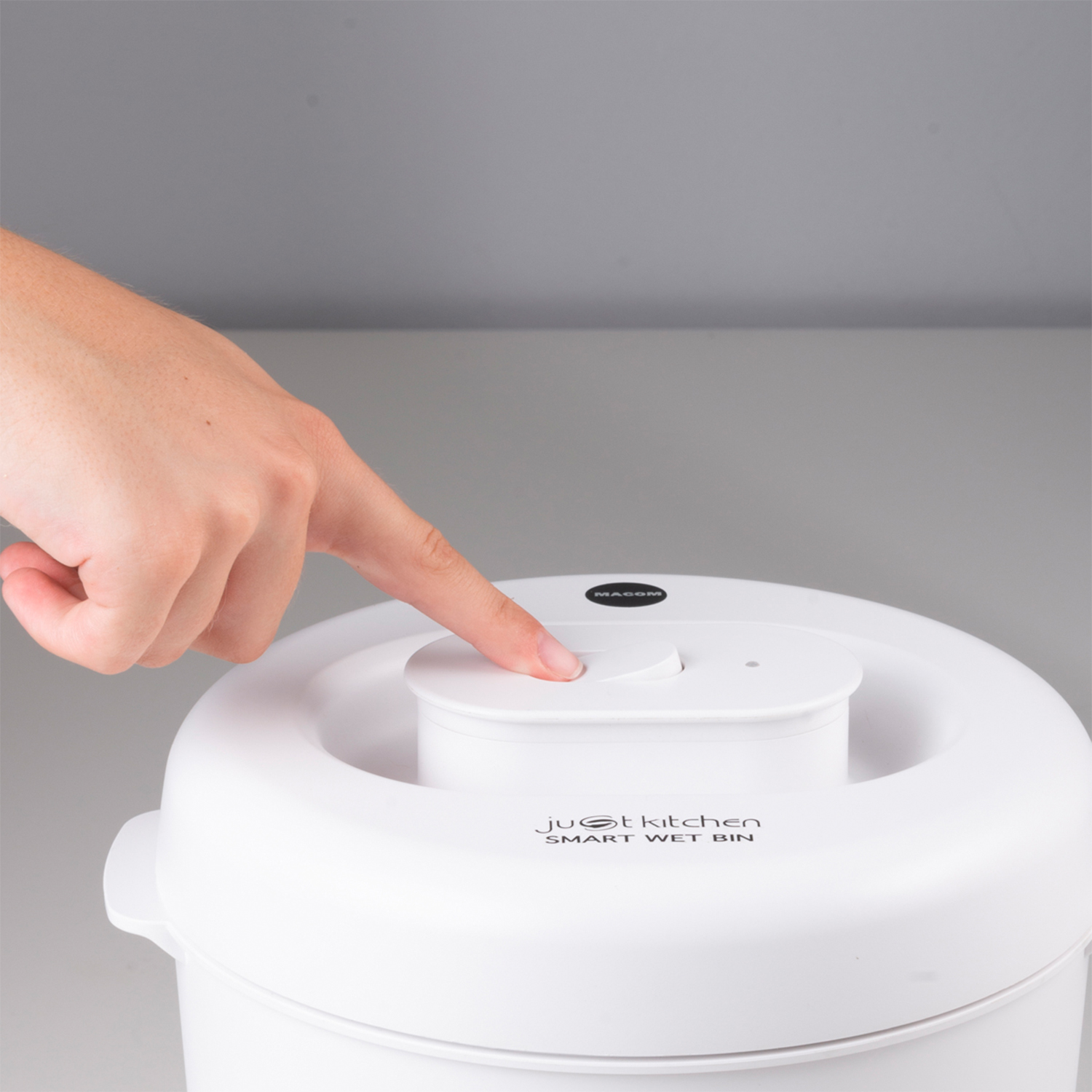 Mano che preme un pulsante bianco su un bidone della cucina intelligente bianco.