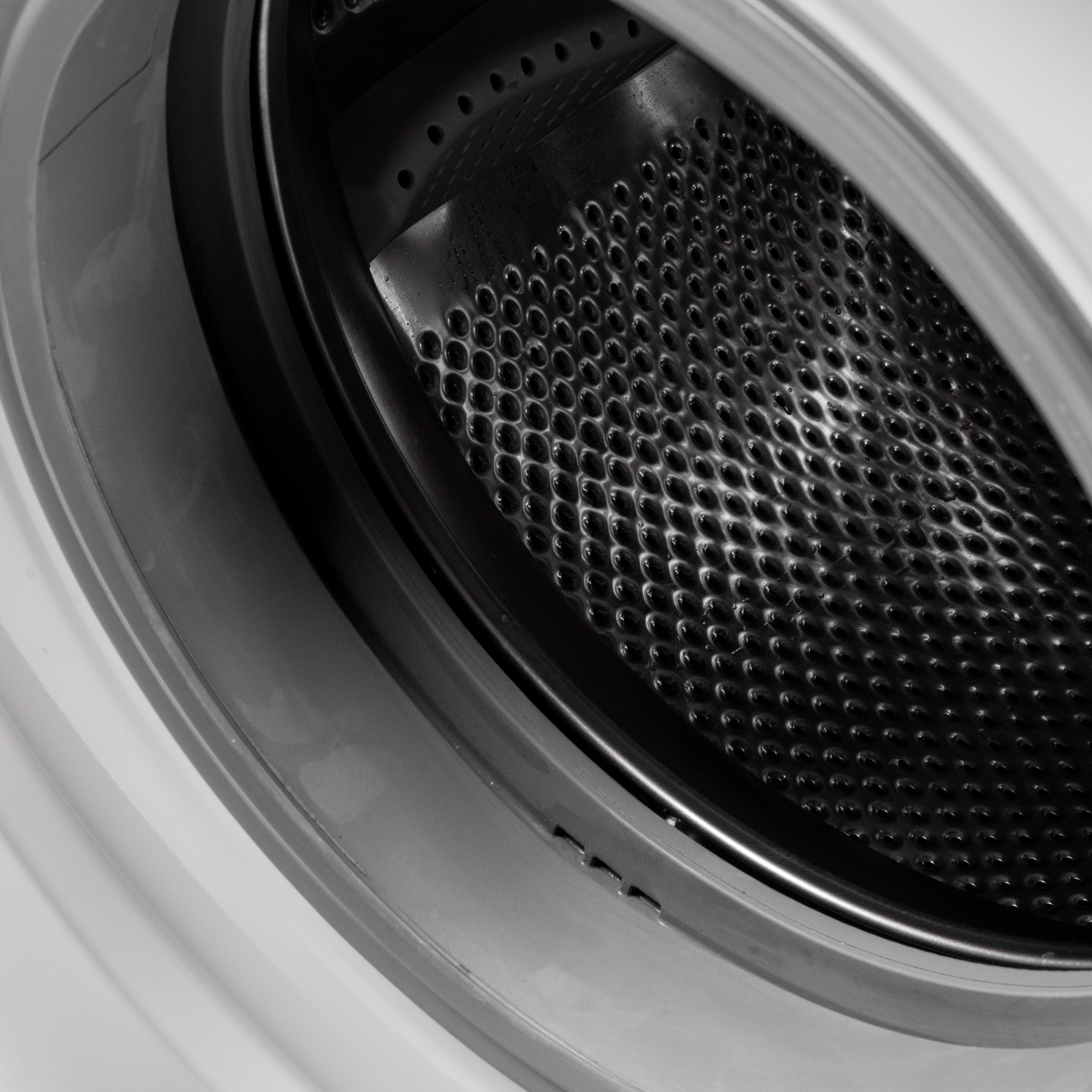 Gros plan sur le tambour d'une machine à laver, montrant l'intérieur en métal perforé et le boîtier blanc et gris environnant.