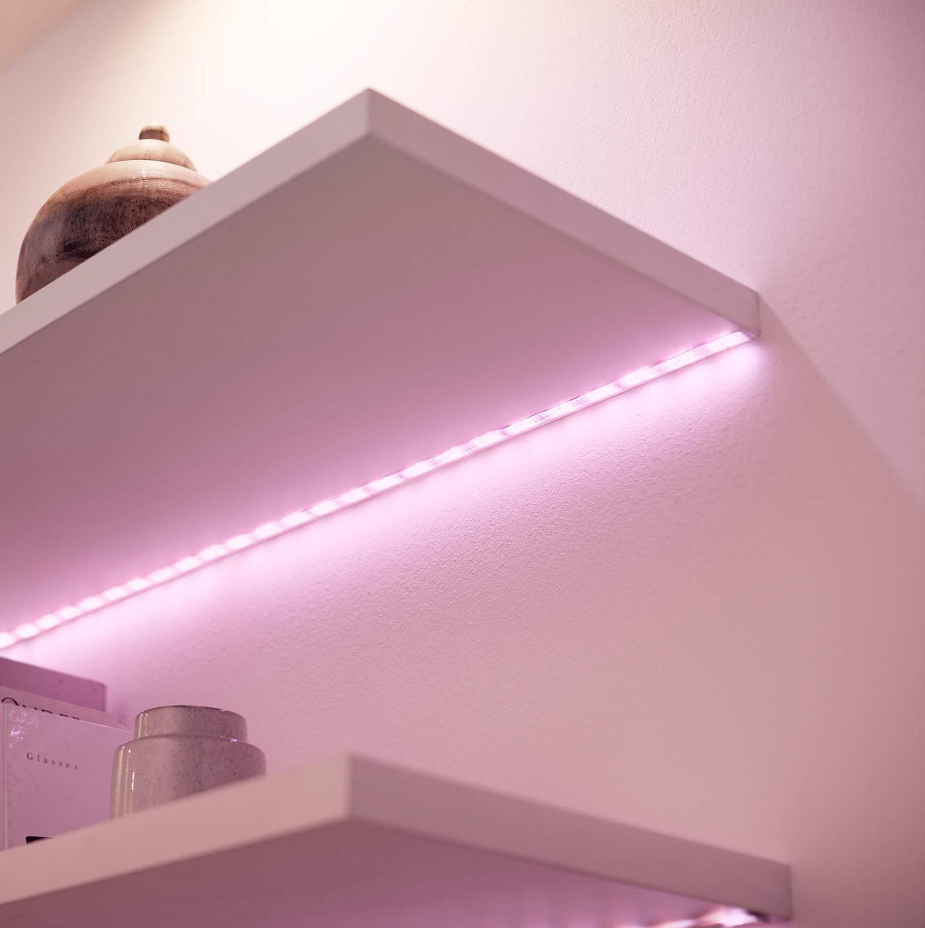Mensole bianche con una striscia luminosa rosa che illumina la parete.