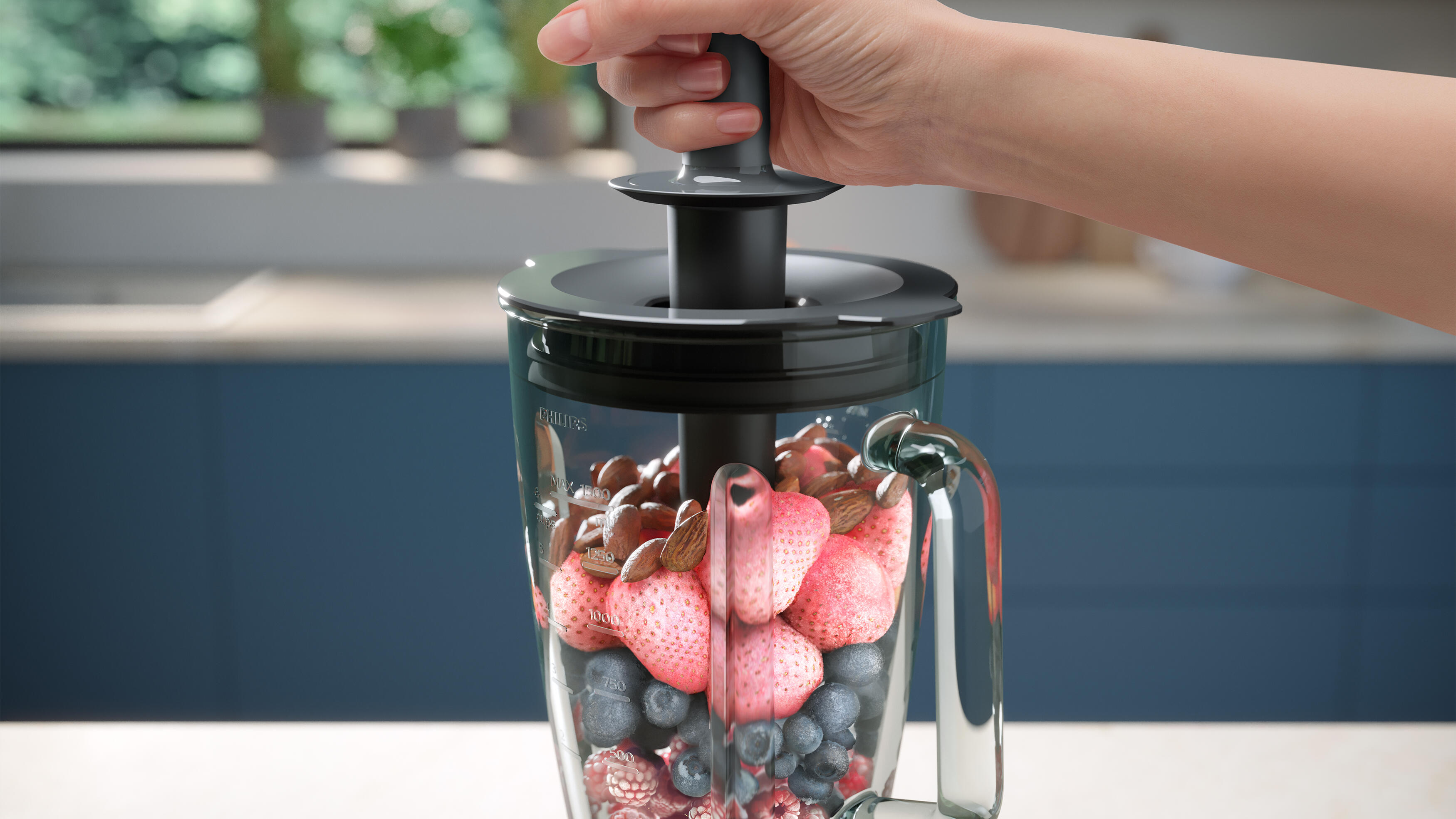 Mano agregando ingredientes a una licuadora con frutas y nueces dentro.