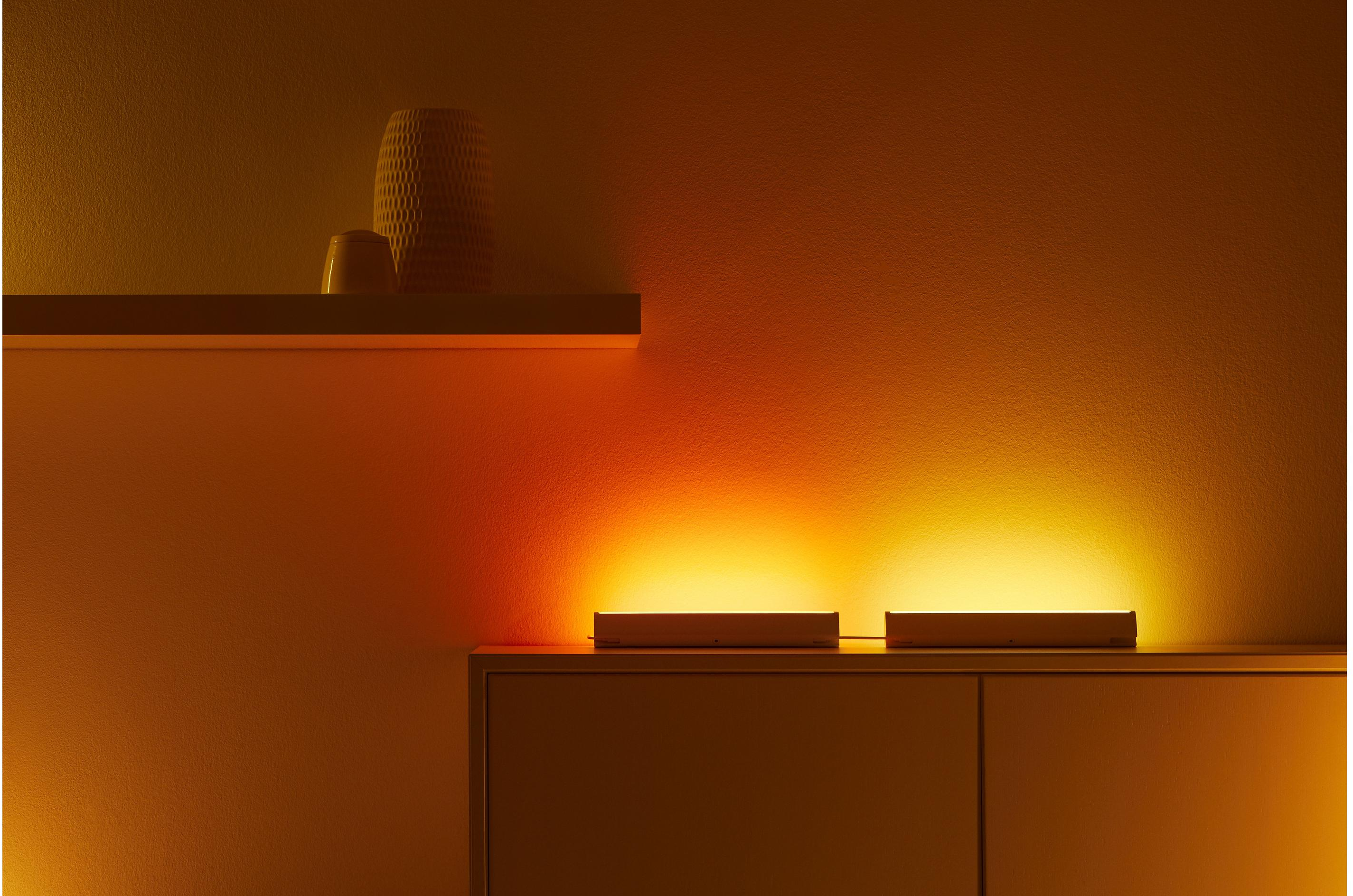 Due barre luminose su una mensola. Il muro dietro è un gradiente di arancione e giallo.