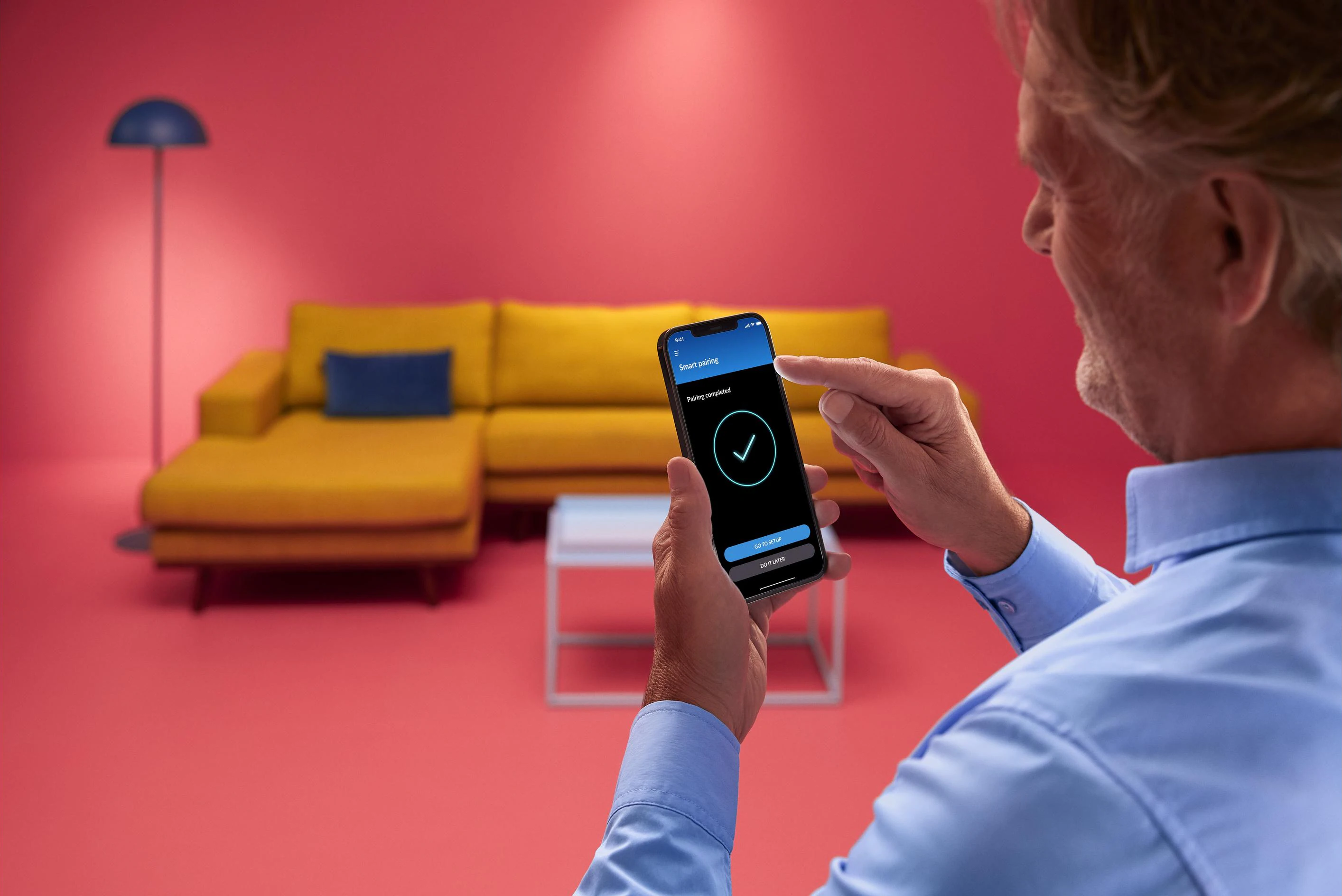 Una persona tiene in mano uno smartphone con un segno di spunta sullo schermo vicino a un divano.
