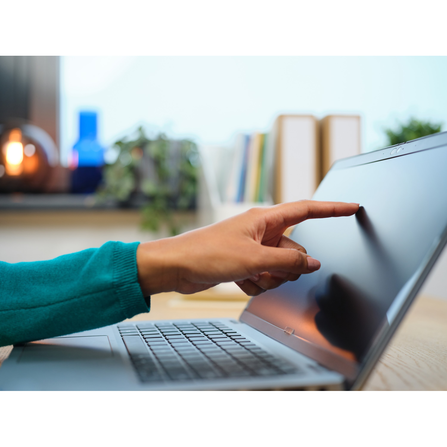 Een hand raakt een laptopscherm aan. Het scherm is donker, de achtergrond is wazig.