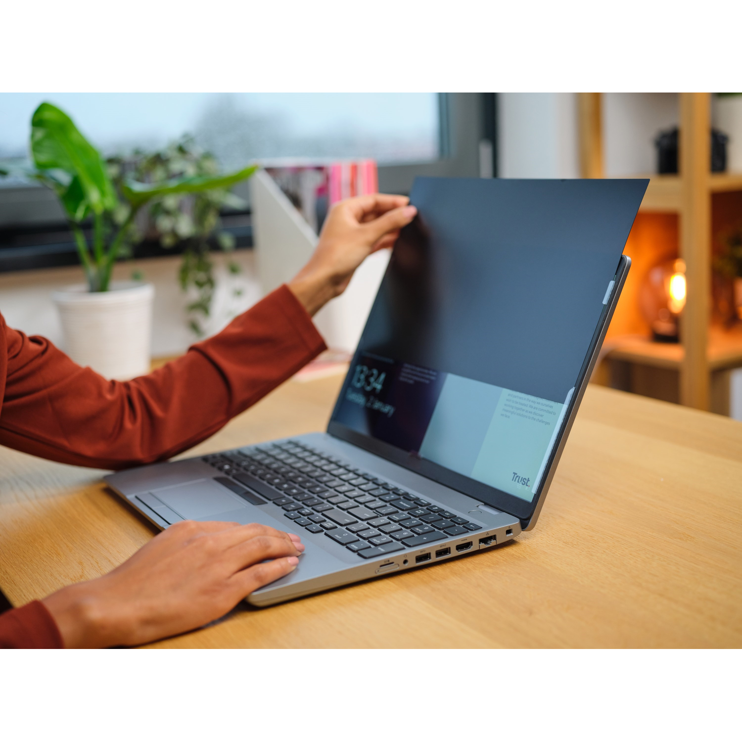 A person's hands holding a black privacy screen over a laptop screen.