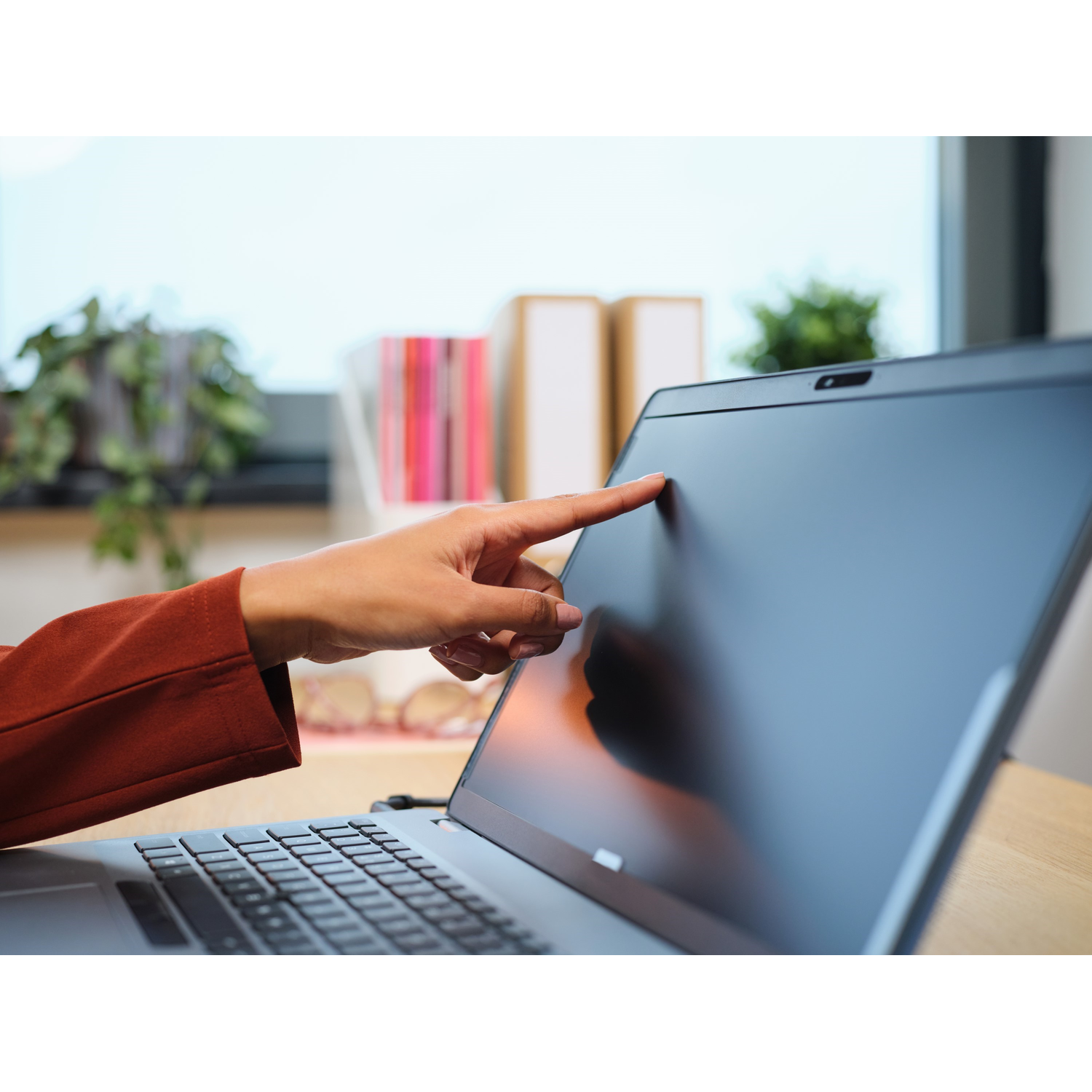 A hand touches a laptop screen. The screen is dark.  A window and desk are in the background.
