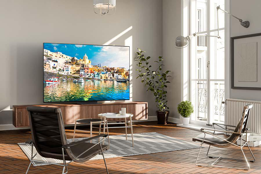 Wohnzimmer mit großem Fernseher, der eine farbenfrohe Meereslandschaft zeigt. Stühle, Pflanzen und ein Teppich sind im Raum.