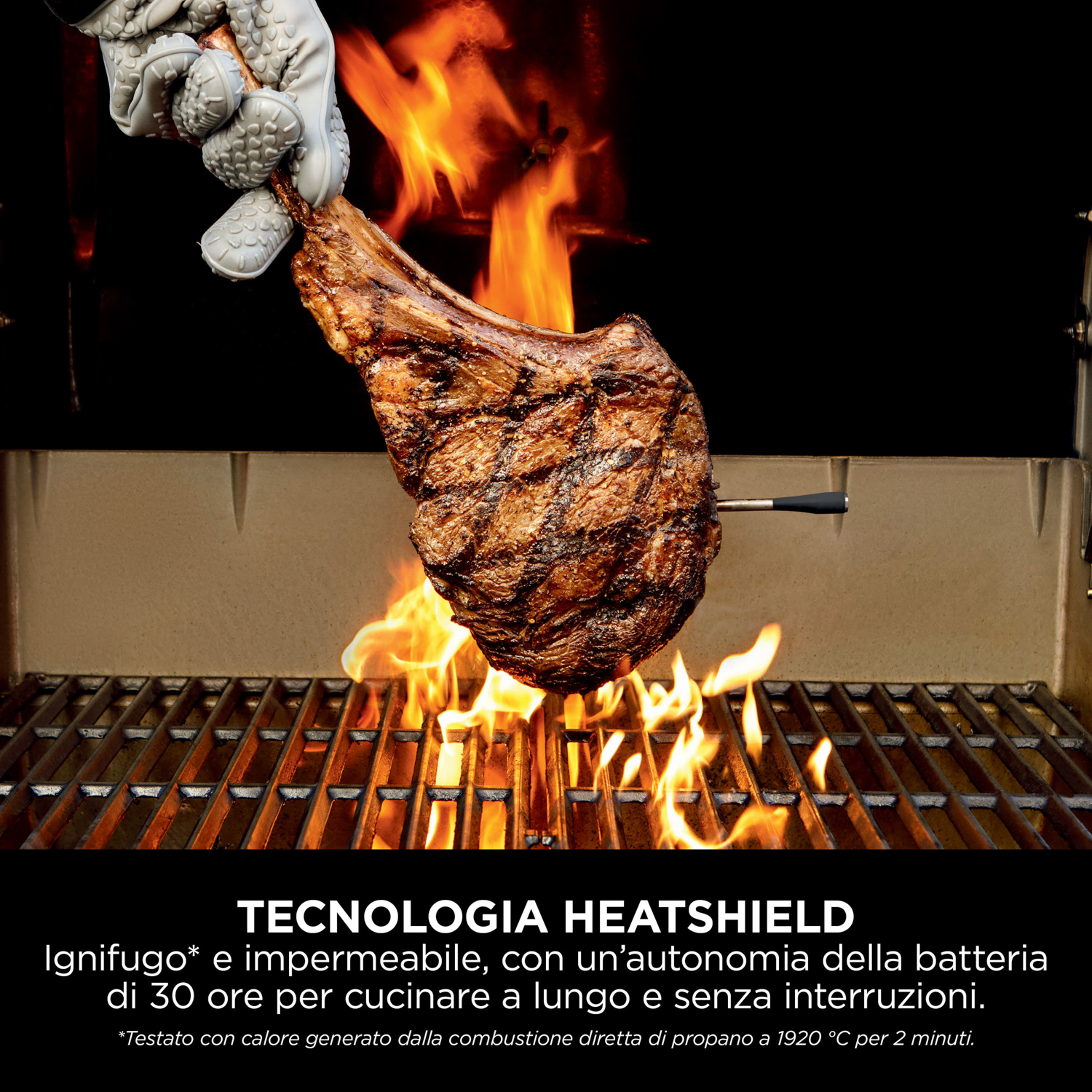 Una bistecca tomahawk in cottura su una griglia con fiamme, tenuta da una mano guantata. Testo sulla tecnologia Heatshield.