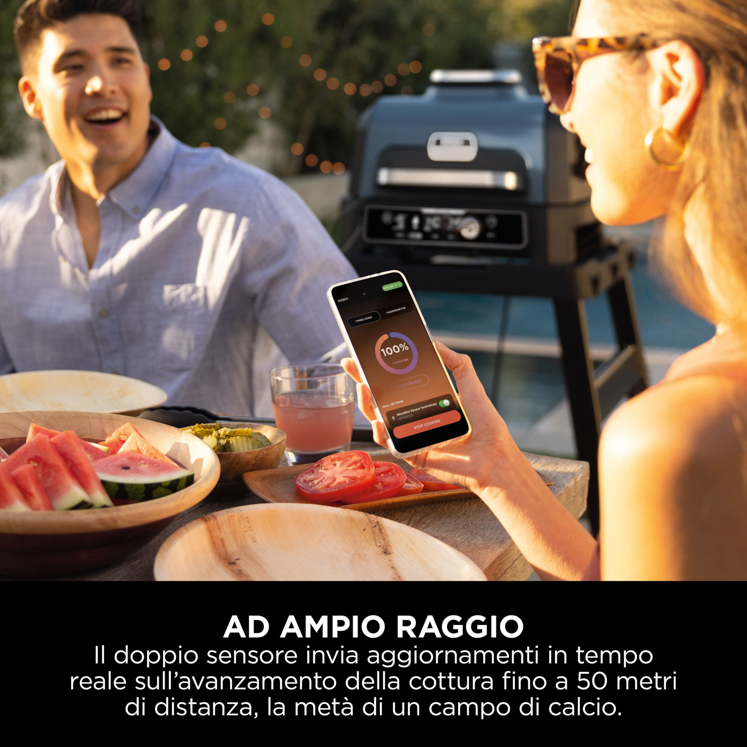 Una donna tiene in mano un telefono che mostra un timer di cottura. Un uomo e cibo sullo sfondo.