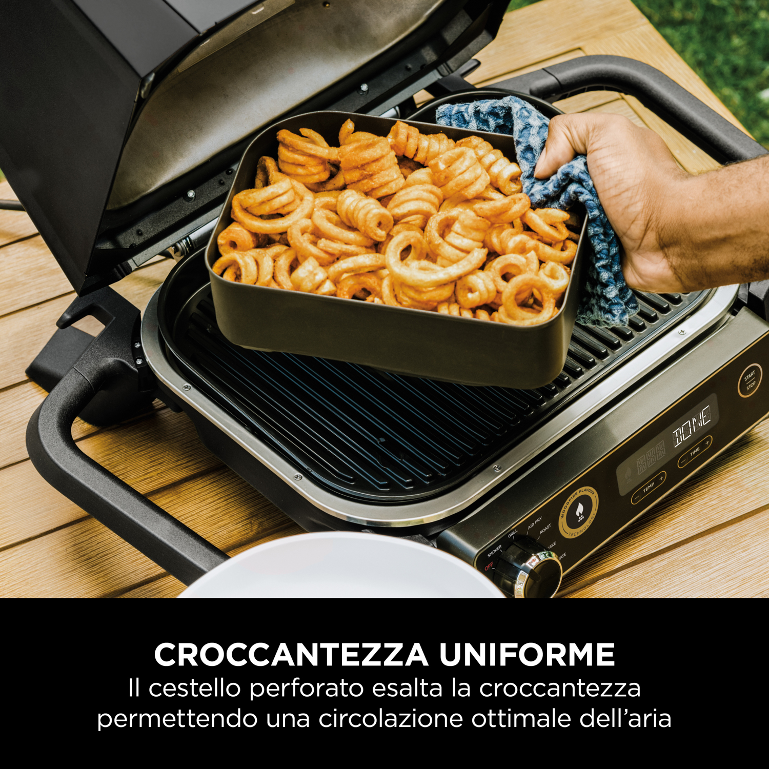 Griglia con un cestello di patatine fritte ricci. Una mano tiene un panno blu. Testo: croccantezza uniforme.